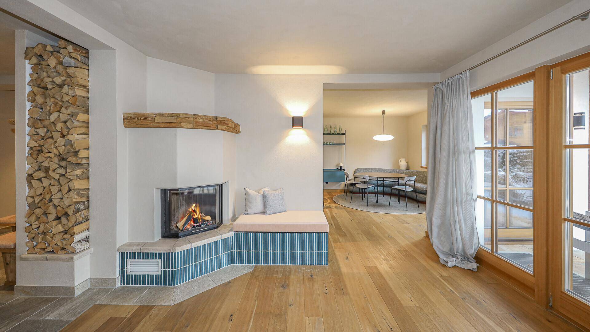 Heller Wohnbereich mit Kamin, Holzlager und offenem Übergang zum angrenzenden Essbereich.