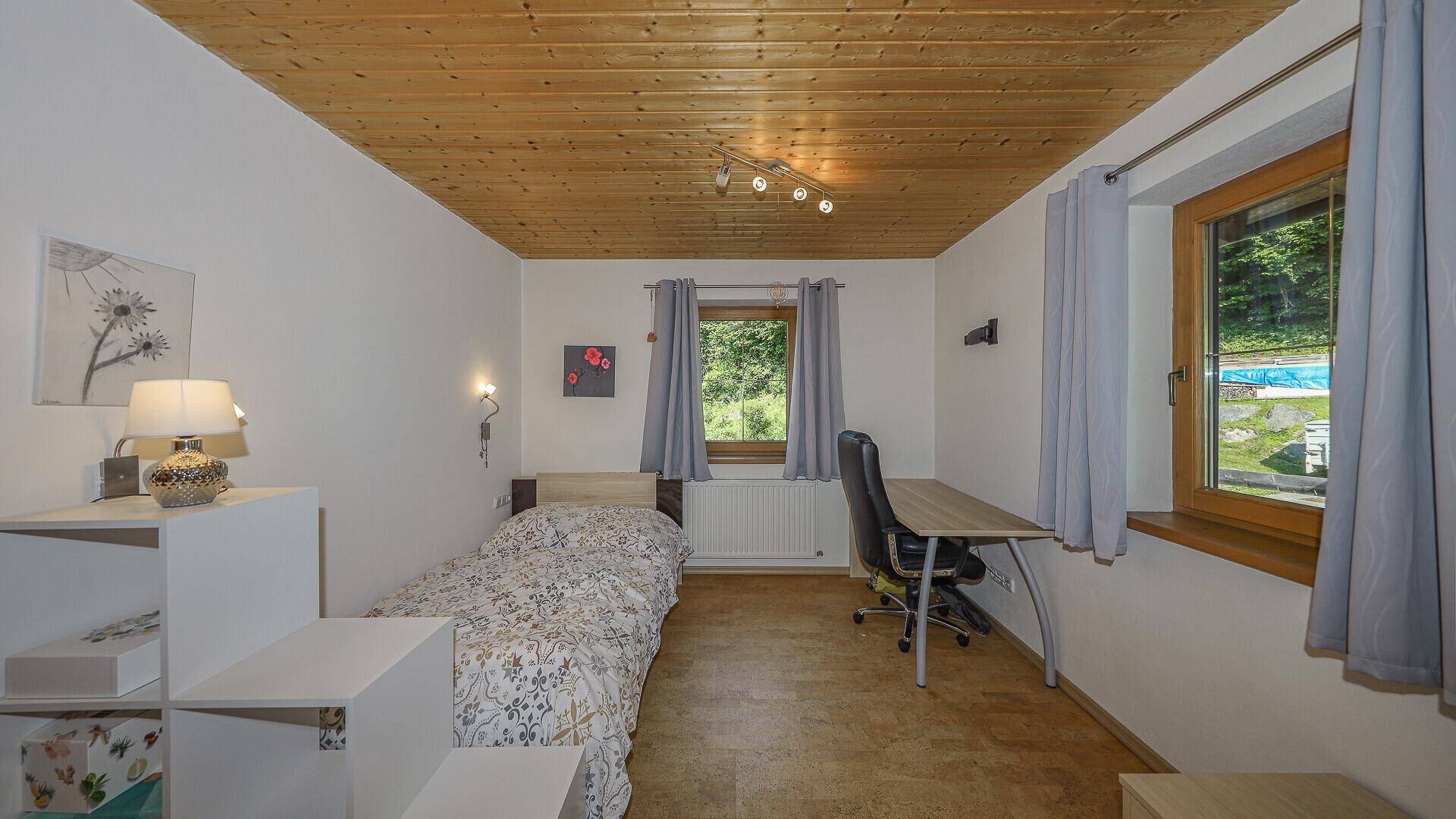 Schlafzimmer mit Einzelbett, Holzdecke und Schreibtisch, ideal als Gäste- oder Kinderzimmer.