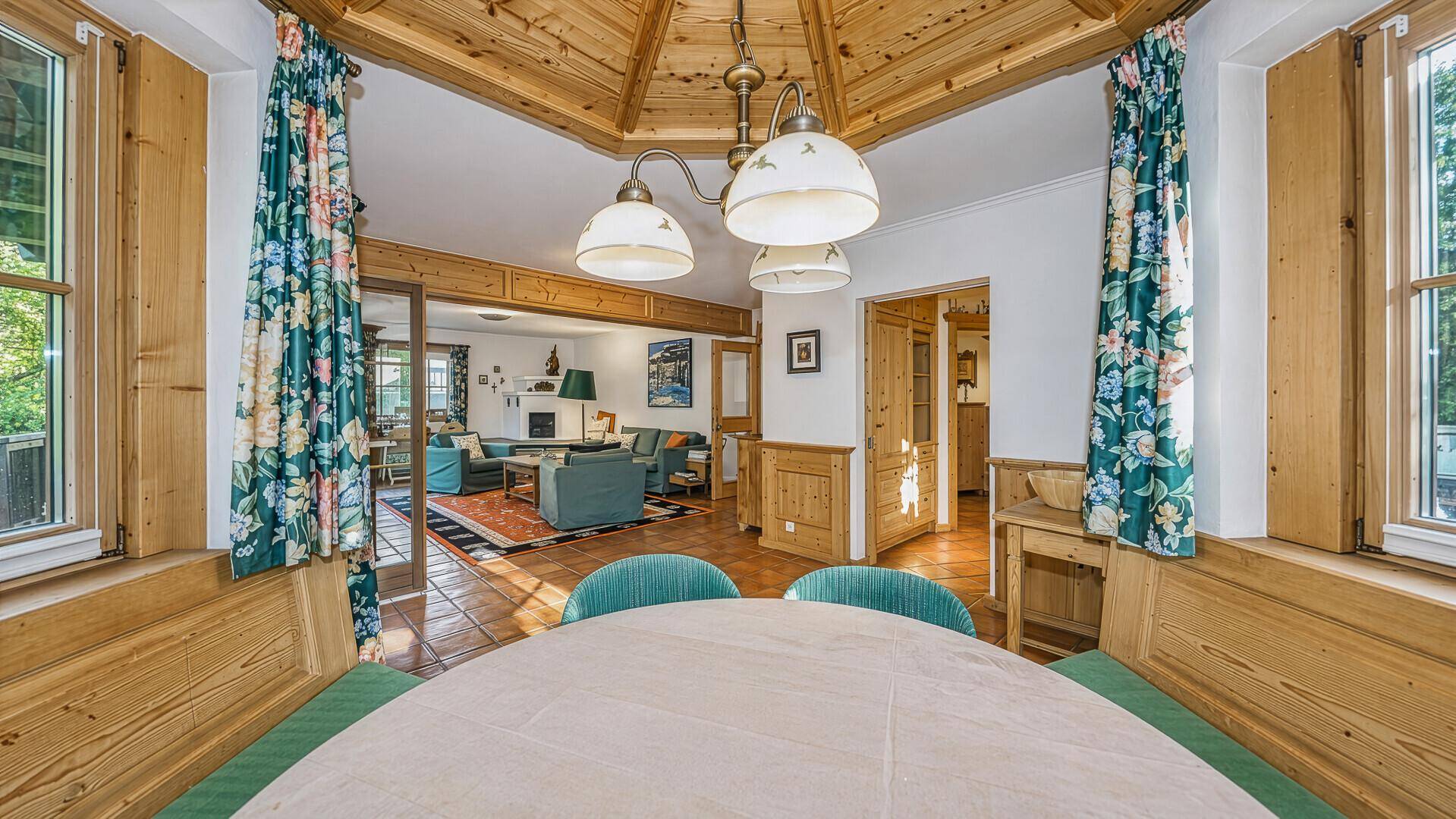 Blick von der Essecke in den traditionellen Wohnbereich mit Kachelofen und rustikalen Möbeln.