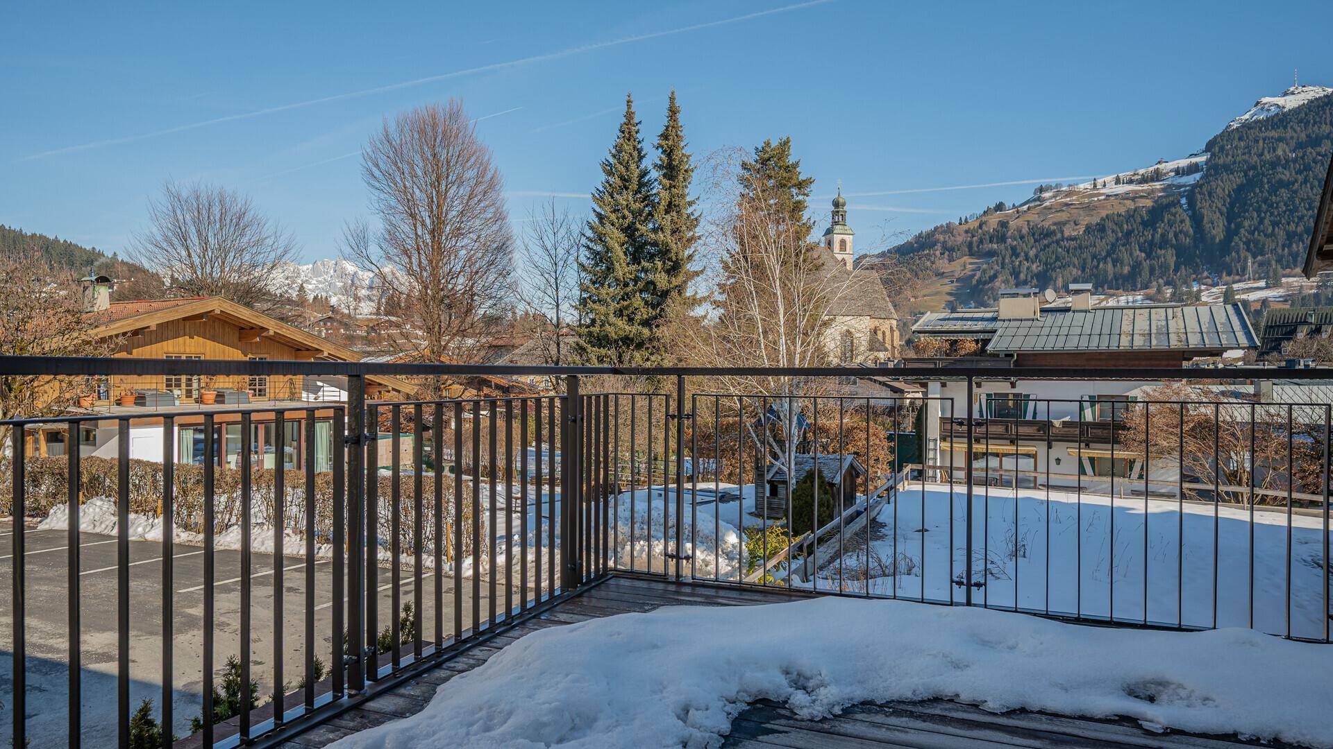 Balkon mit Blick auf die verschneite Umgebung, Berge und die Kirche im Dorfzentrum.