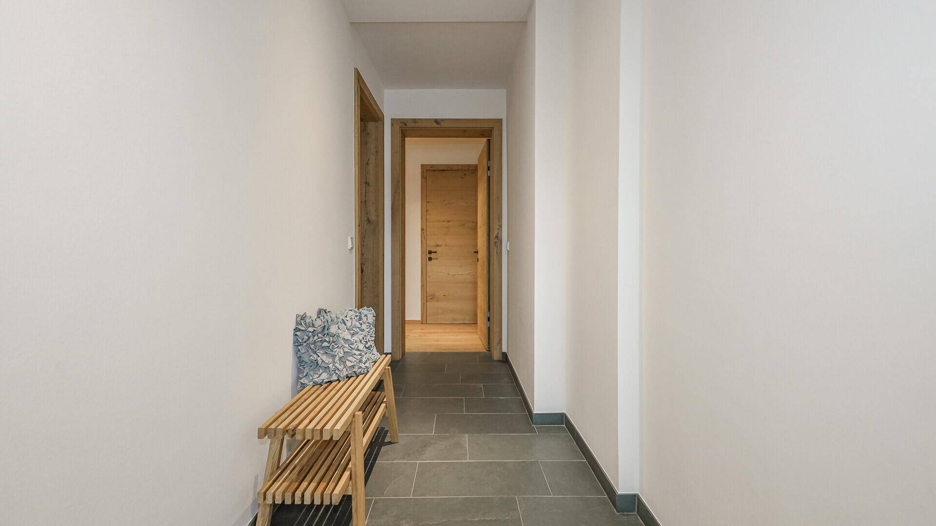 Schmaler Flur mit dunklem Fliesenboden und einer kleinen Holzbank.