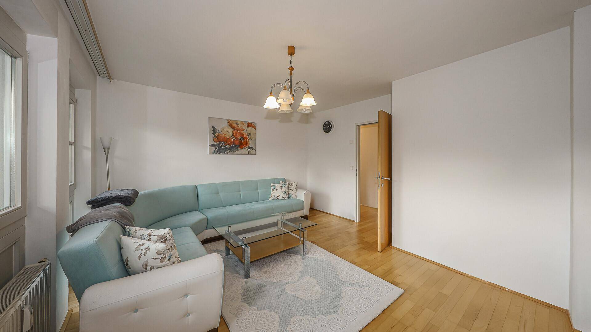 Helles Wohnzimmer mit türkisem Ecksofa, Holzboden und Blick auf die Berge durch die Fenster.
