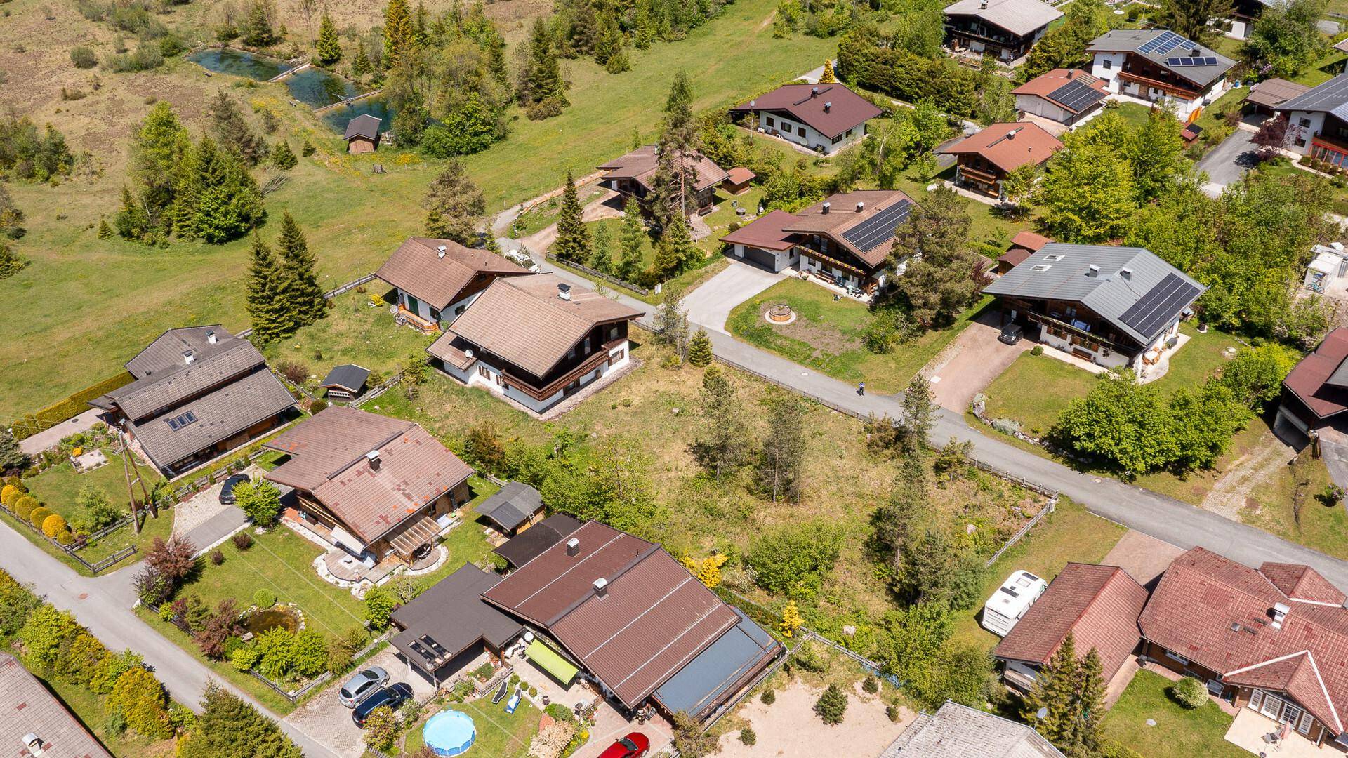 Weitläufige Luftaufnahme einer Wohnsiedlung mit vielen Häusern und grünen Gärten in den Bergen.