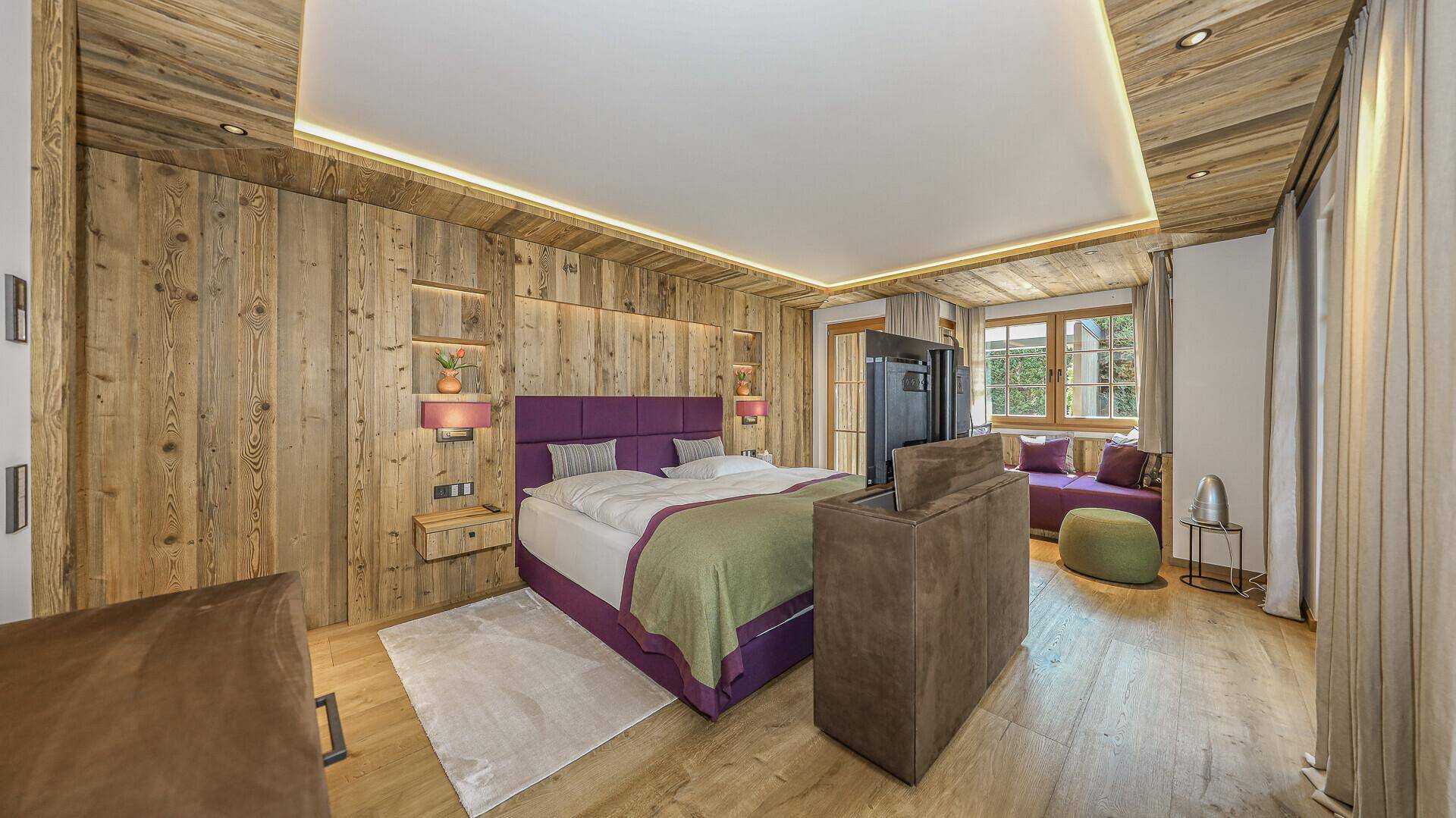 Gemütliches Schlafzimmer mit Holzwänden, lila Akzenten und einem bequemen Bett mit Blick ins Grüne.