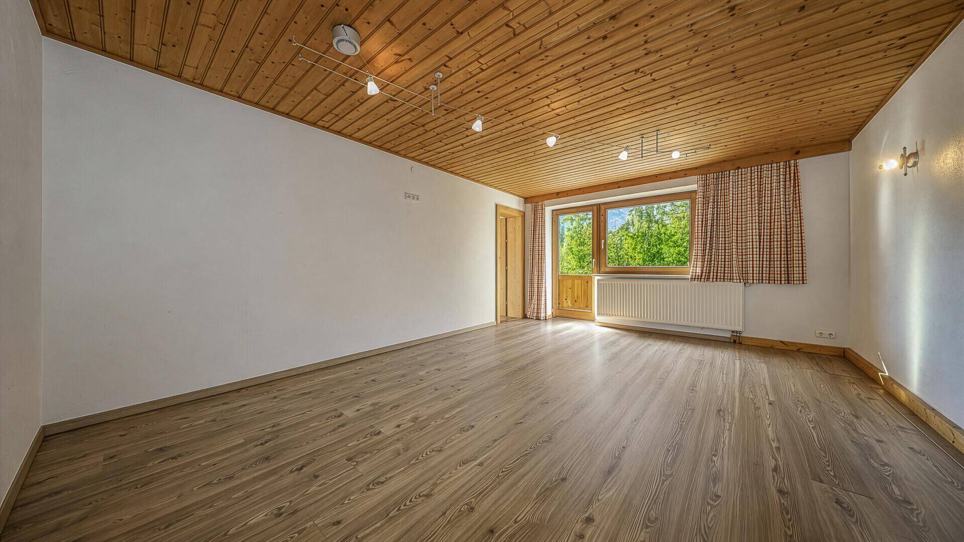 Geräumiger Wohnraum mit Holzbalkendecke, Laminatboden und Zugang zum Balkon.
