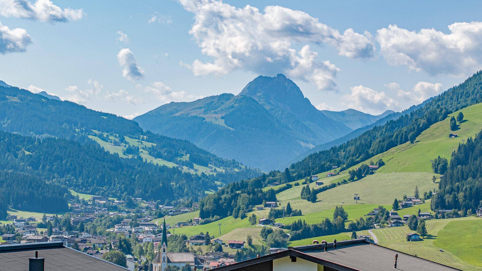 Atemberaubender Blick auf ein malerisches Tal mit einem Dorf und imposanten Bergen im Hintergrund.