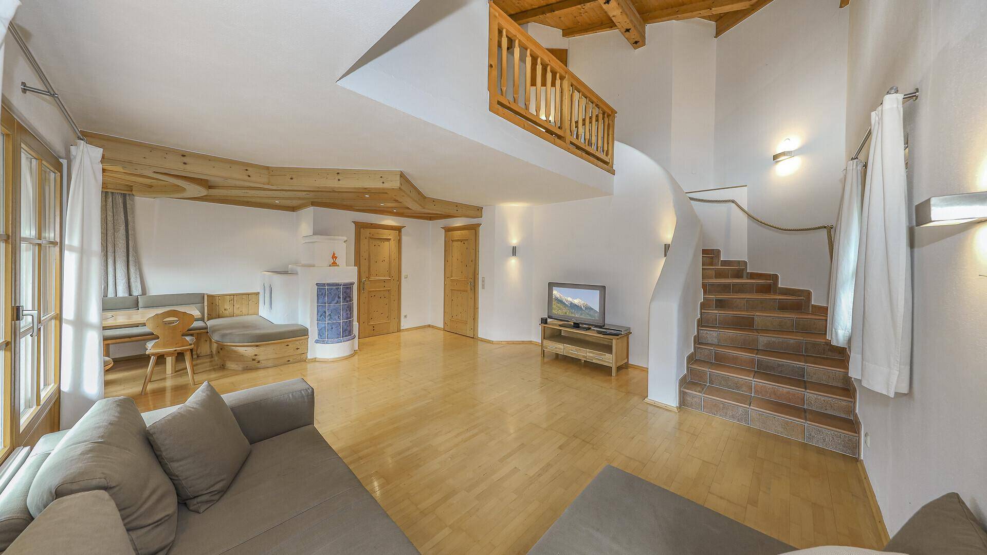 Geräumiges Wohnzimmer mit Holzbalkendecke, Kachelofen und Treppe zur oberen Etage.