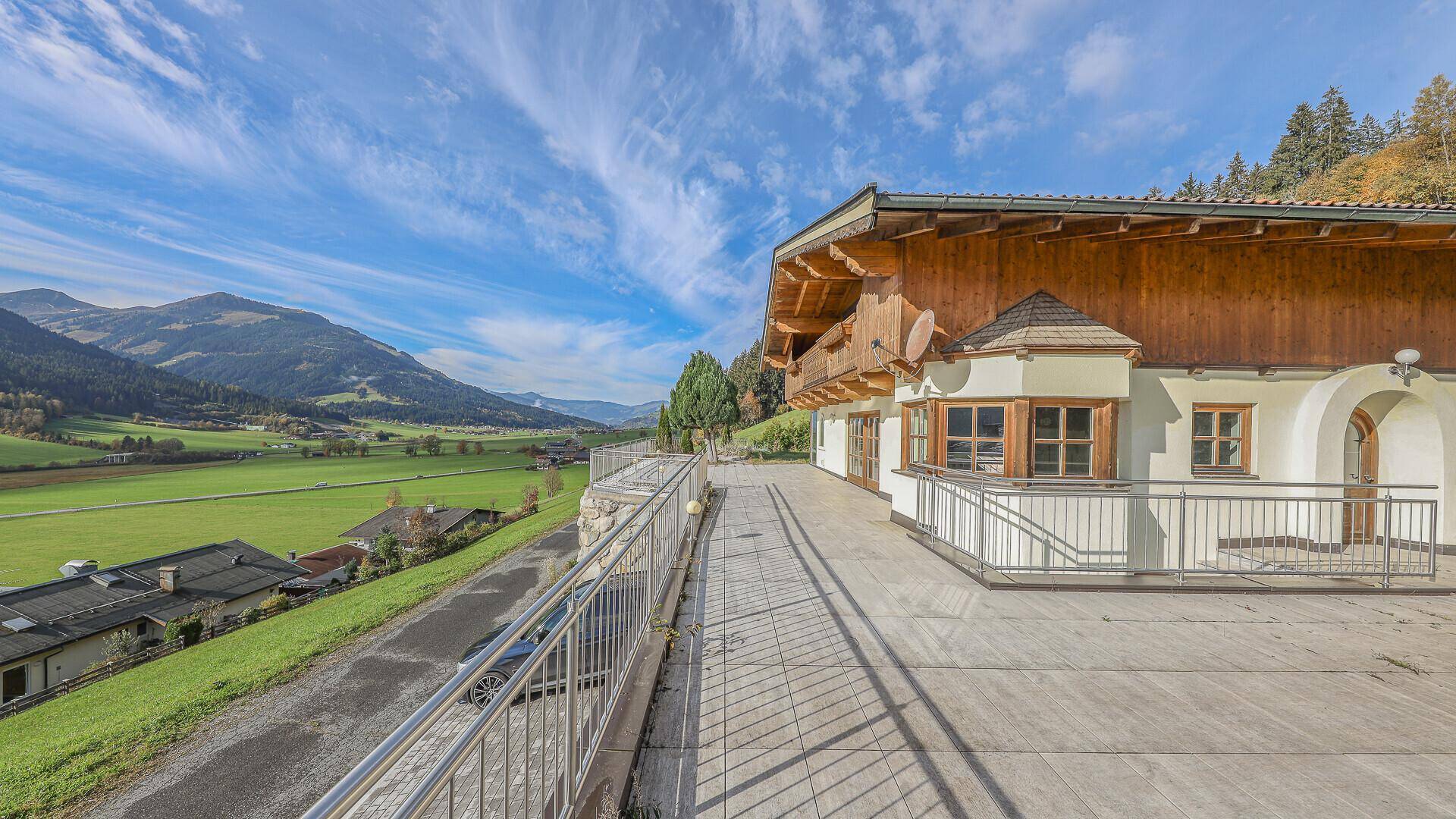 Lange Terrasse entlang der Hausfassade mit Blick auf die grüne Landschaft und die Berge.