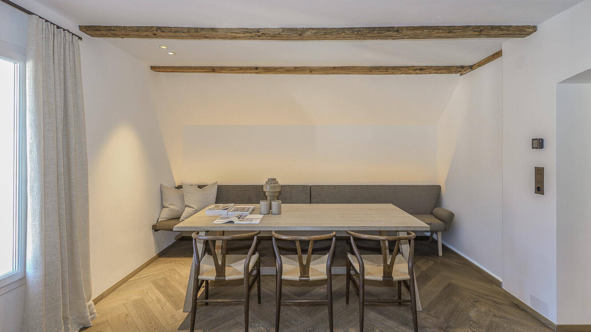 Gemütlicher Essbereich mit Holztisch, Sitzbank und sichtbaren Holzbalken.