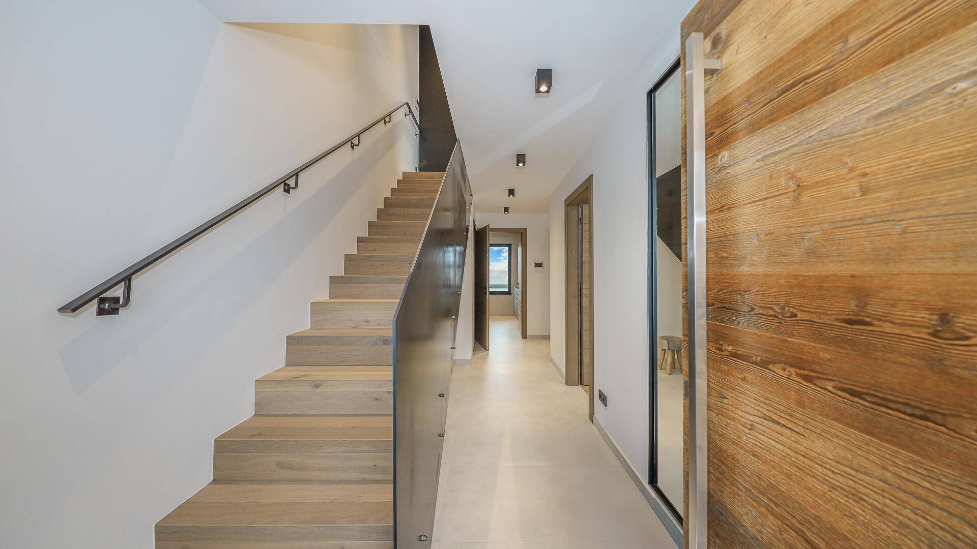 Heller Flur mit Holztreppe, Glasgeländer und modernen Holztüren.