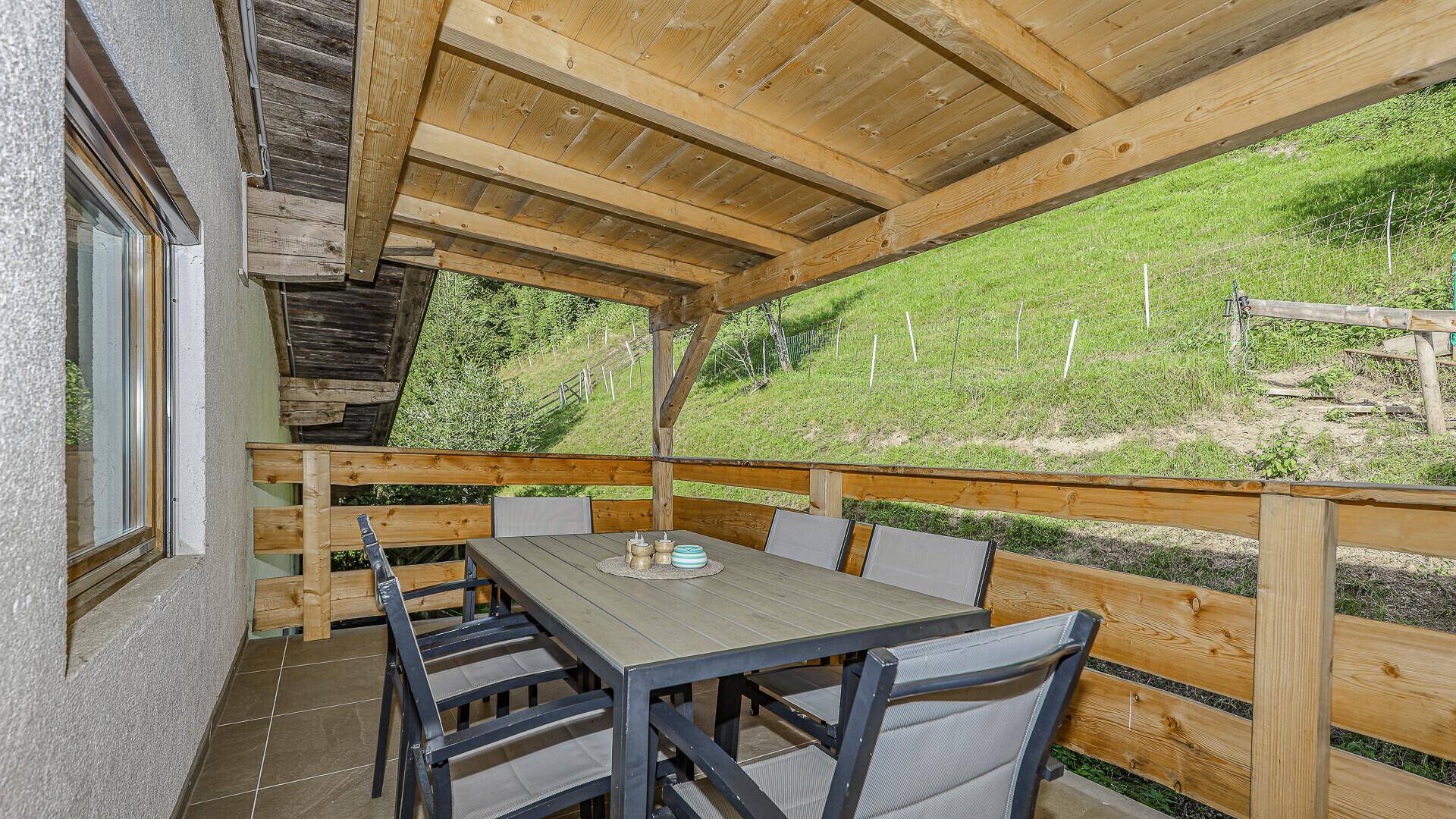 Überdachte Terrasse mit großem Esstisch und Stühlen, ideal für Mahlzeiten im Freien mit Blick ins Grüne.