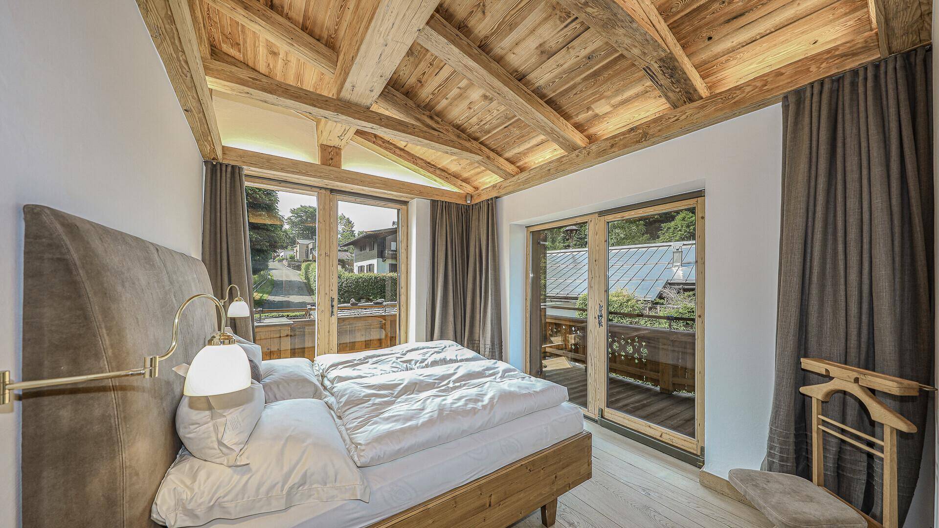 Gemütliches Schlafzimmer mit Holzbalkendecke, Balkonzugang und Blick ins Grüne.
