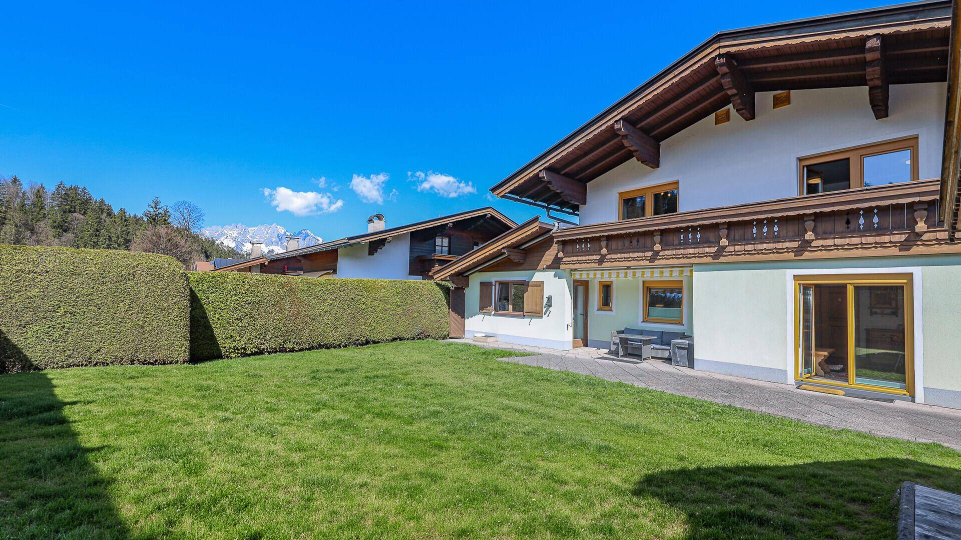 Weitläufiger Garten mit Rasenfläche und Hecke, umgeben von alpiner Landschaft.