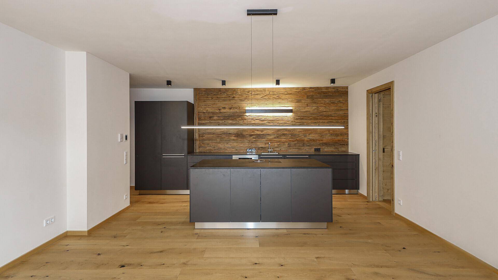 Moderne Küche mit dunklen Schränken, Kücheninsel und Holzwand.