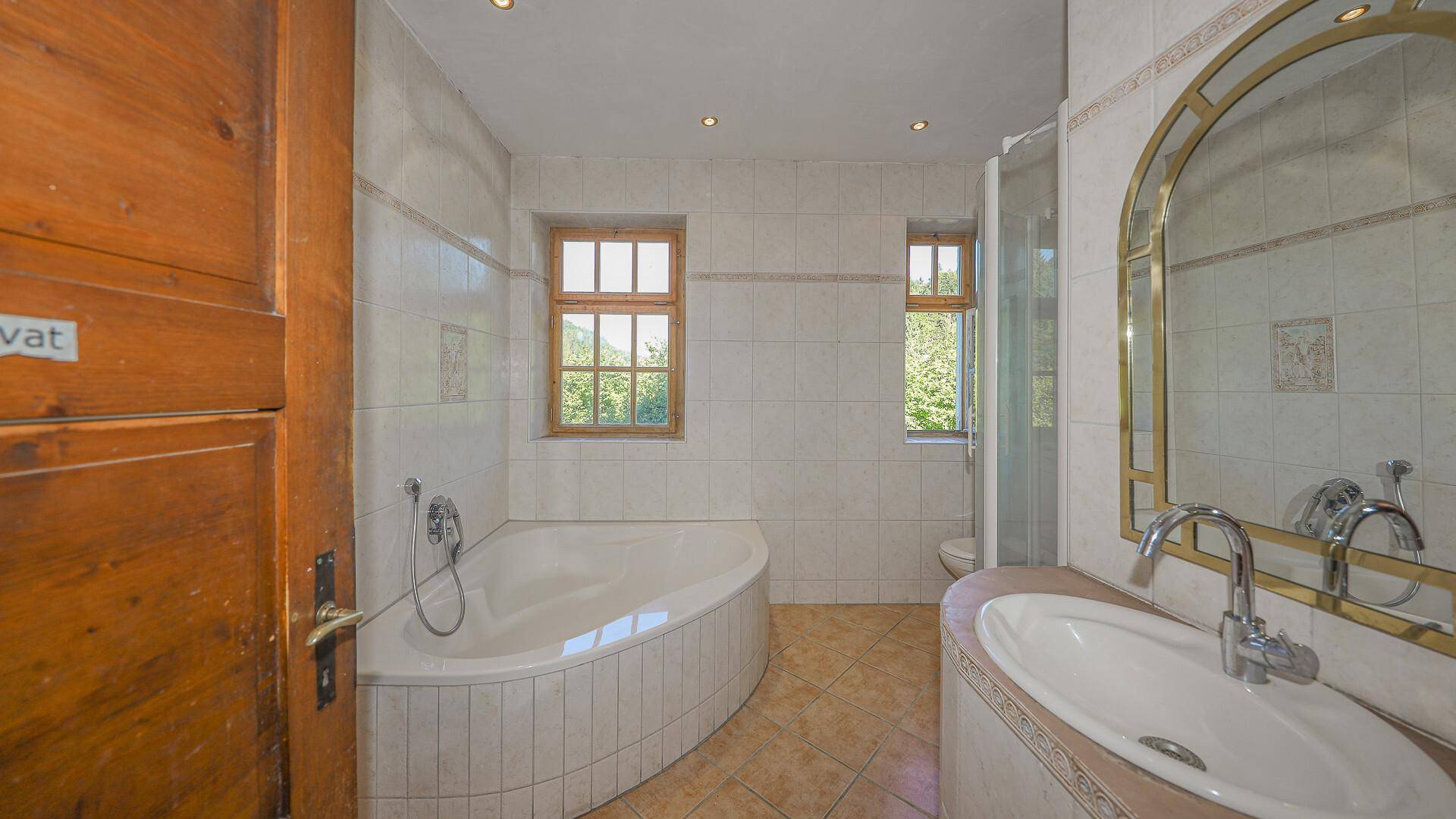 Badezimmer mit Eckbadewanne, Dusche, Einzelwaschbecken und Fenstern für Tageslicht.