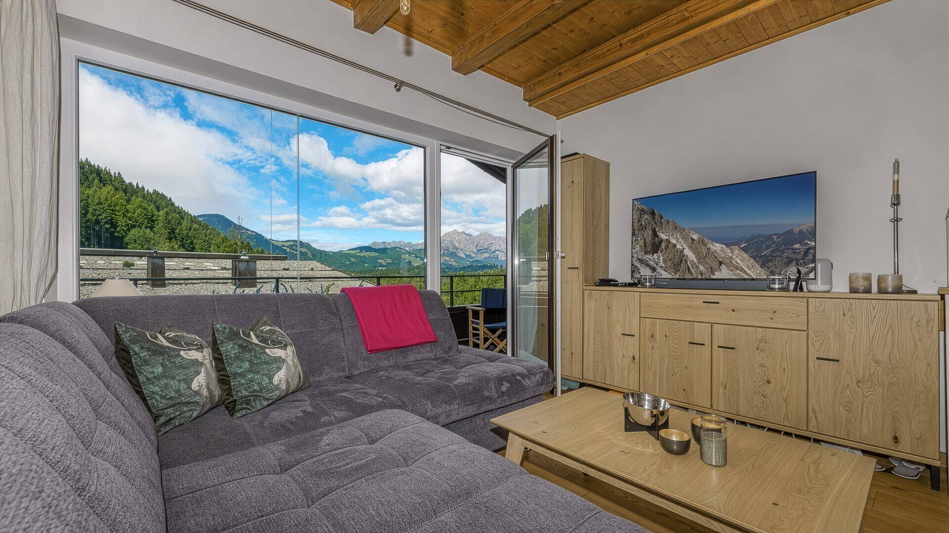 Helles Wohnzimmer mit großem Fenster, Holzbalkendecke und beeindruckendem Bergblick.
