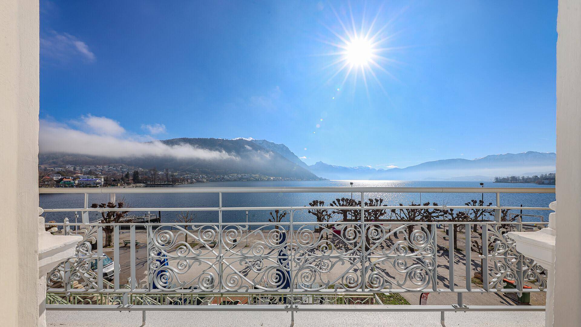 Sonniger Balkon mit schmiedeeisernem Geländer und weitem Blick über den See und die Berge.