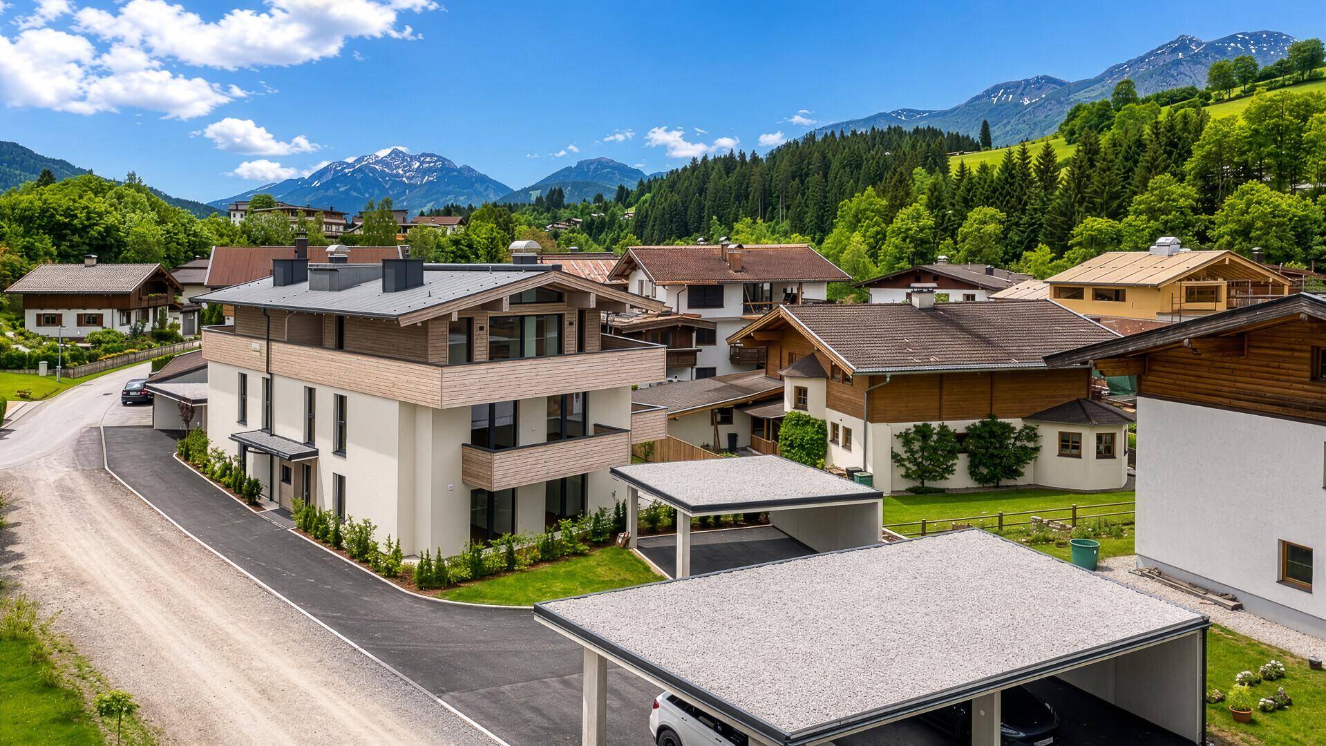 Moderne Wohnanlage mit Carports, umgeben von Natur und Berglandschaft.