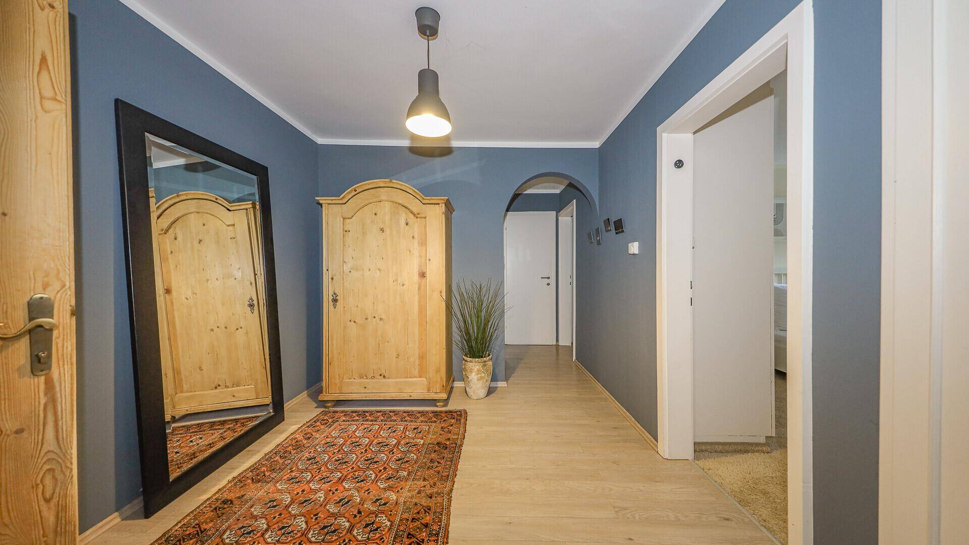 Geräumiger Flur mit Holzschrank, großem Spiegel und blauen Wänden.