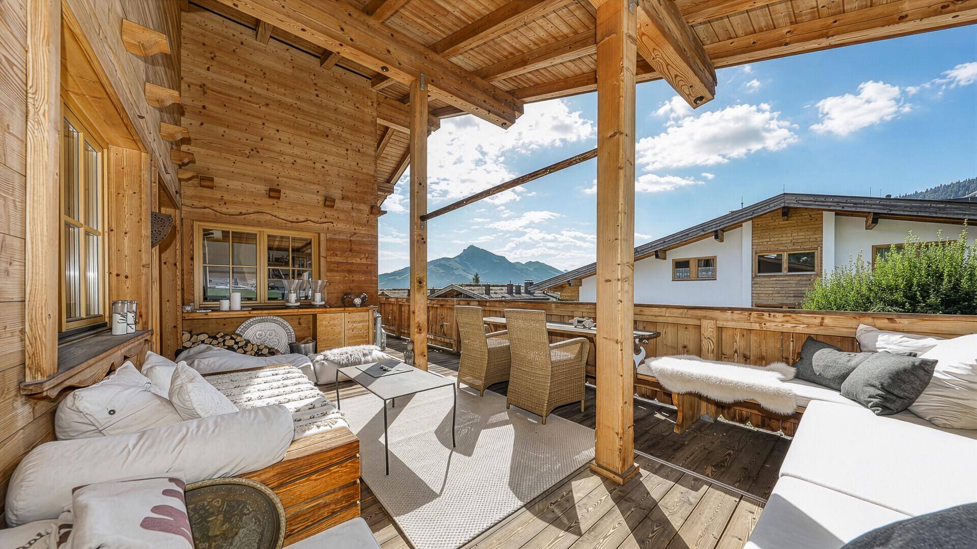 Großer überdachter Holzbalkon mit gemütlicher Sitzecke und beeindruckendem Bergblick.