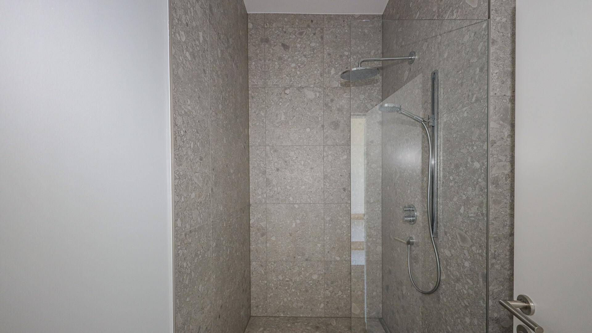 Moderne Dusche mit Glaswand und Regenduschkopf in einem gefliesten Badezimmer.