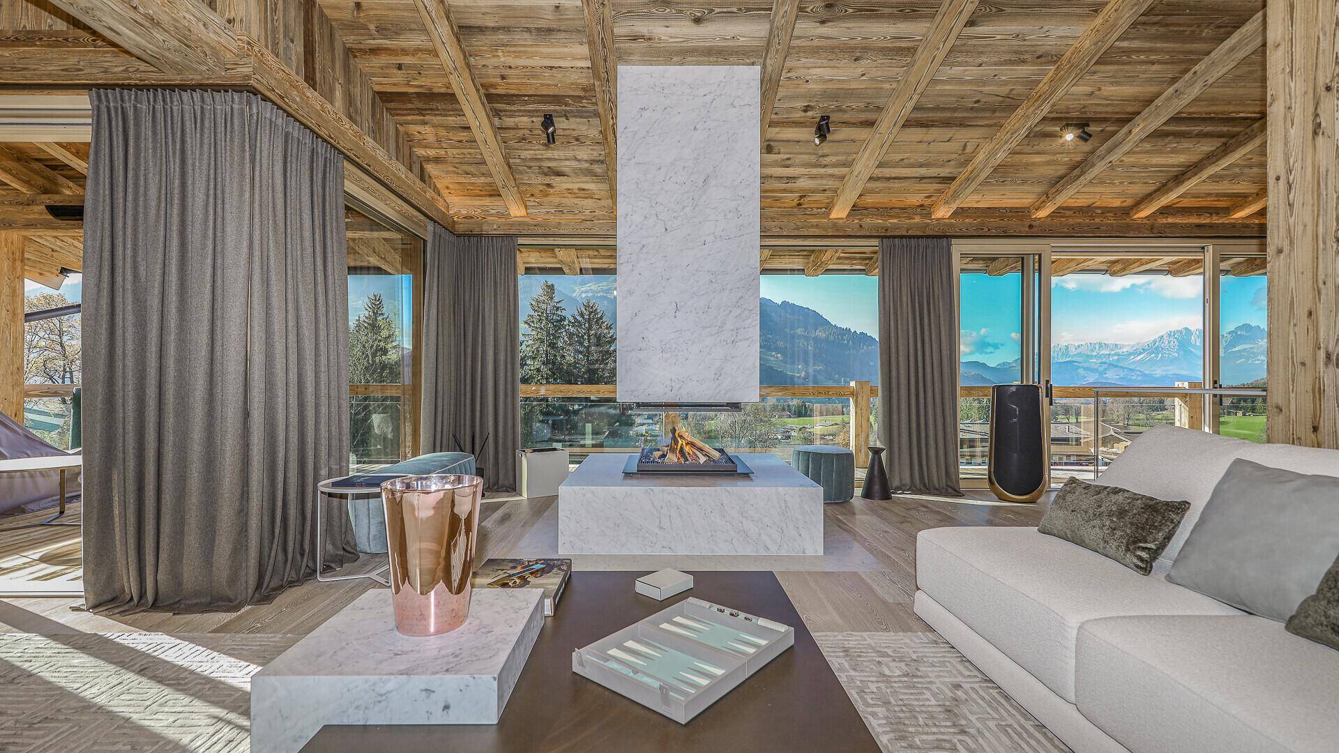 Elegantes Wohnzimmer mit modernem Kamin, Holzbalkendecke und weitem Blick auf die Bergwelt.