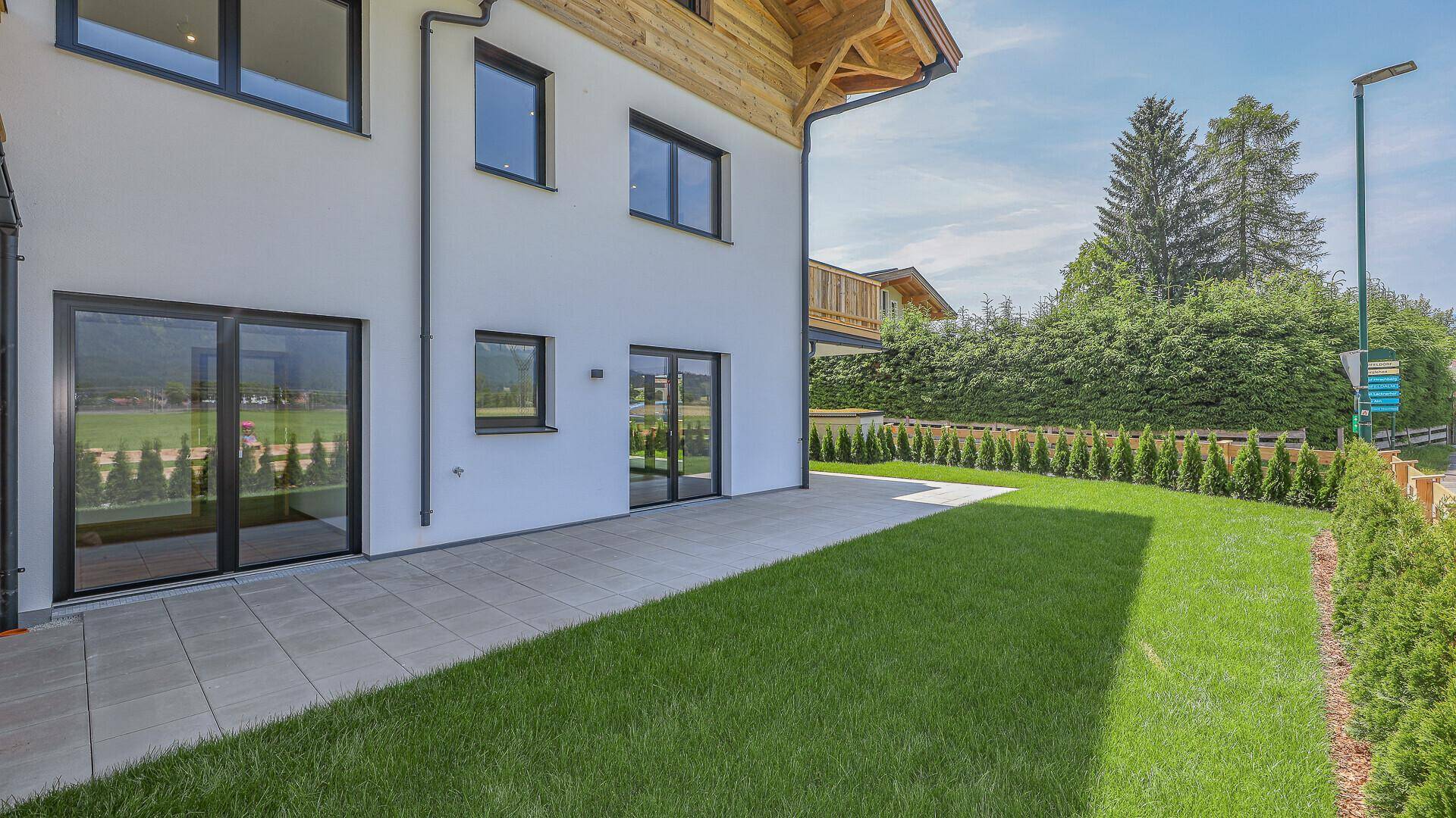 Außenansicht des Gebäudes mit Terrasse, Rasenfläche und Zugang zu den Innenräumen.