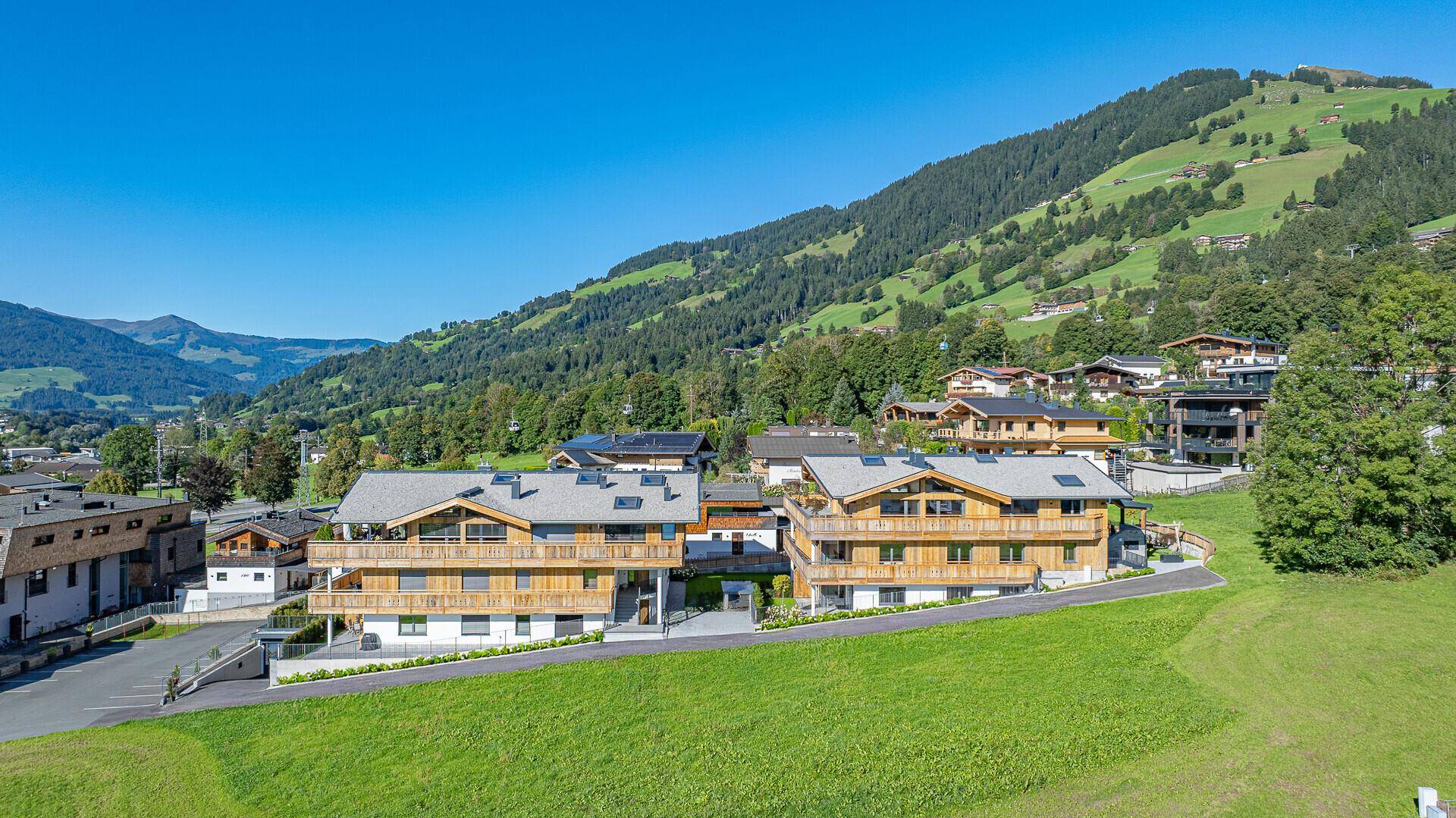 Luftaufnahme von zwei modernen Gebäuden in alpiner Umgebung mit grünen Hügeln.
