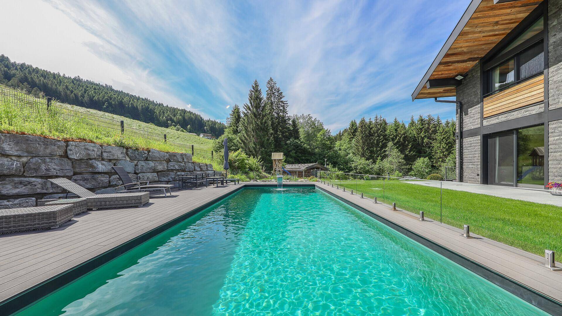 Langer Außenpool mit Holzdeck und Blick auf die umliegende Berglandschaft und den Wald.