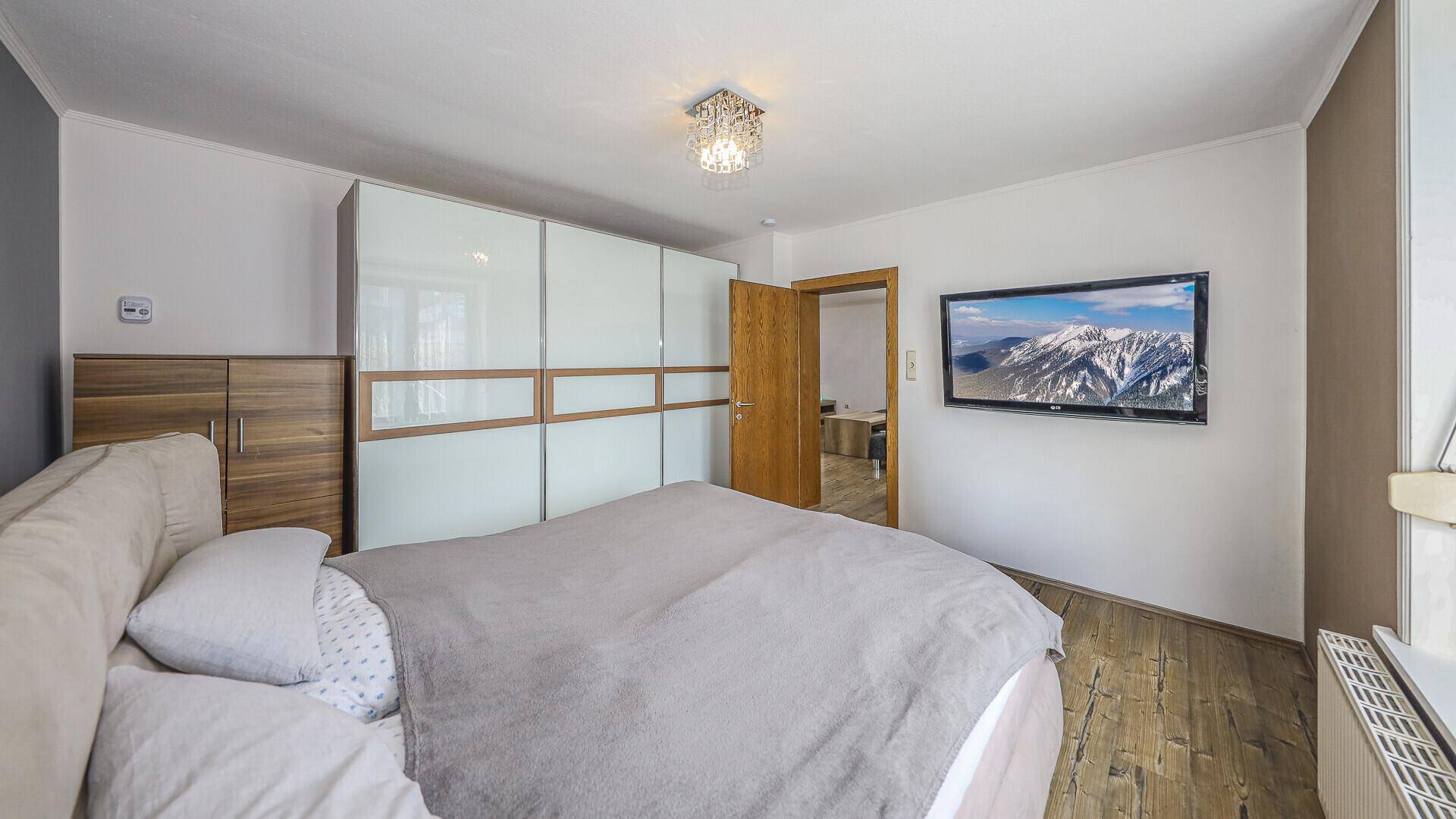 Schlafzimmer mit Doppelbett, großem Einbauschrank und Fernseher an der Wand, mit Holzboden.