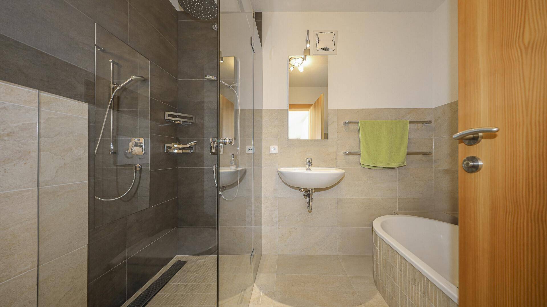 Modernes Badezimmer mit Dusche, Badewanne und hellen Fliesen, gut beleuchtet.