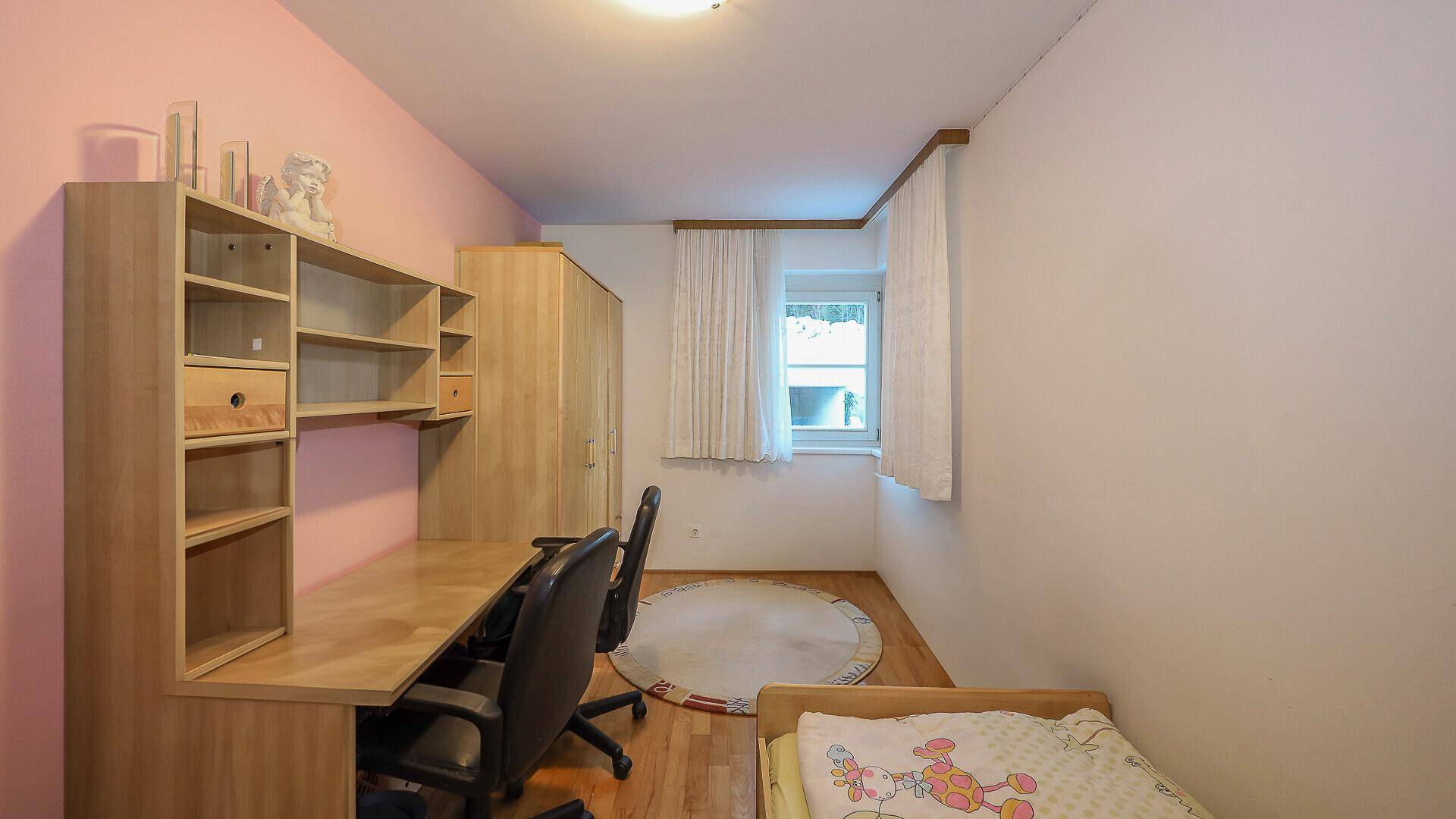 Kinderzimmer oder Büro mit Schreibtisch, Regalen und Fenster, einfach und funktional eingerichtet.