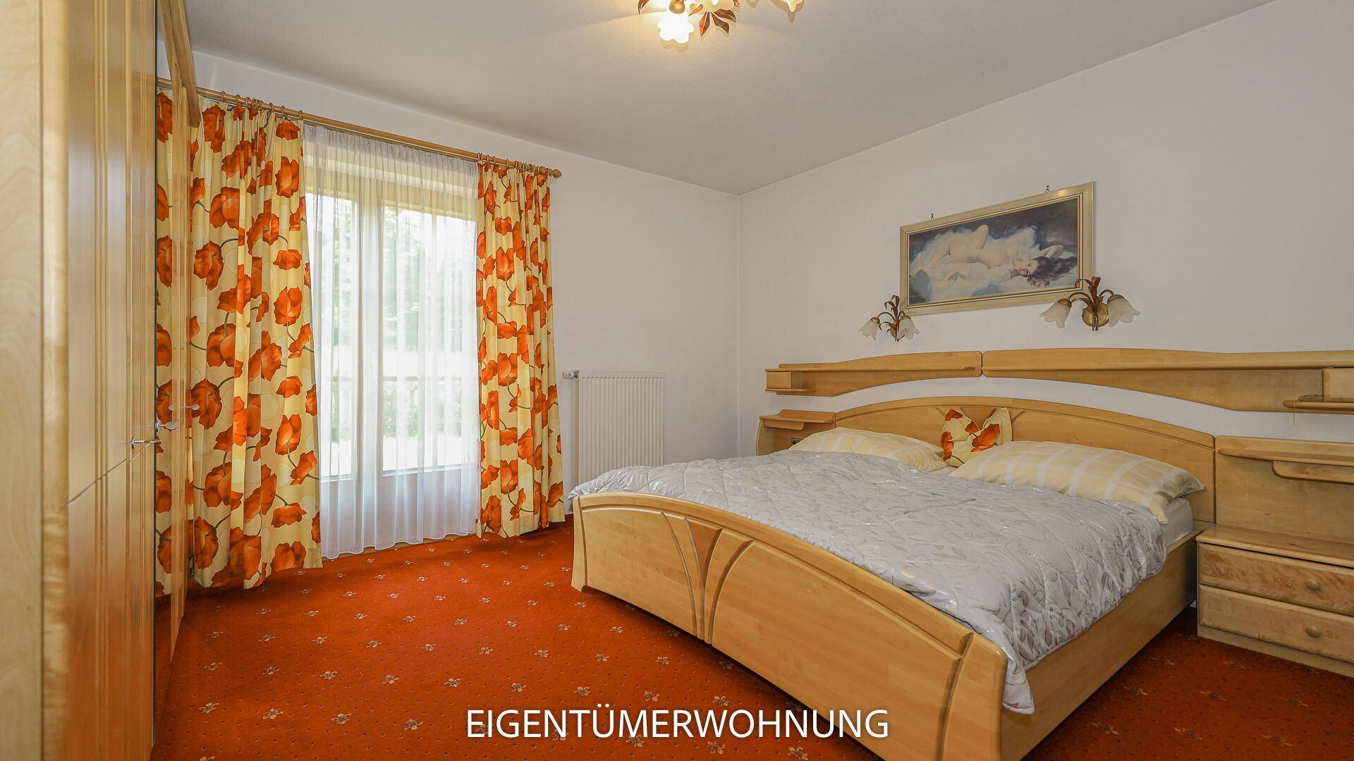 Helles Schlafzimmer mit Doppelbett, Holzmöbeln und farbenfrohem Teppichboden.