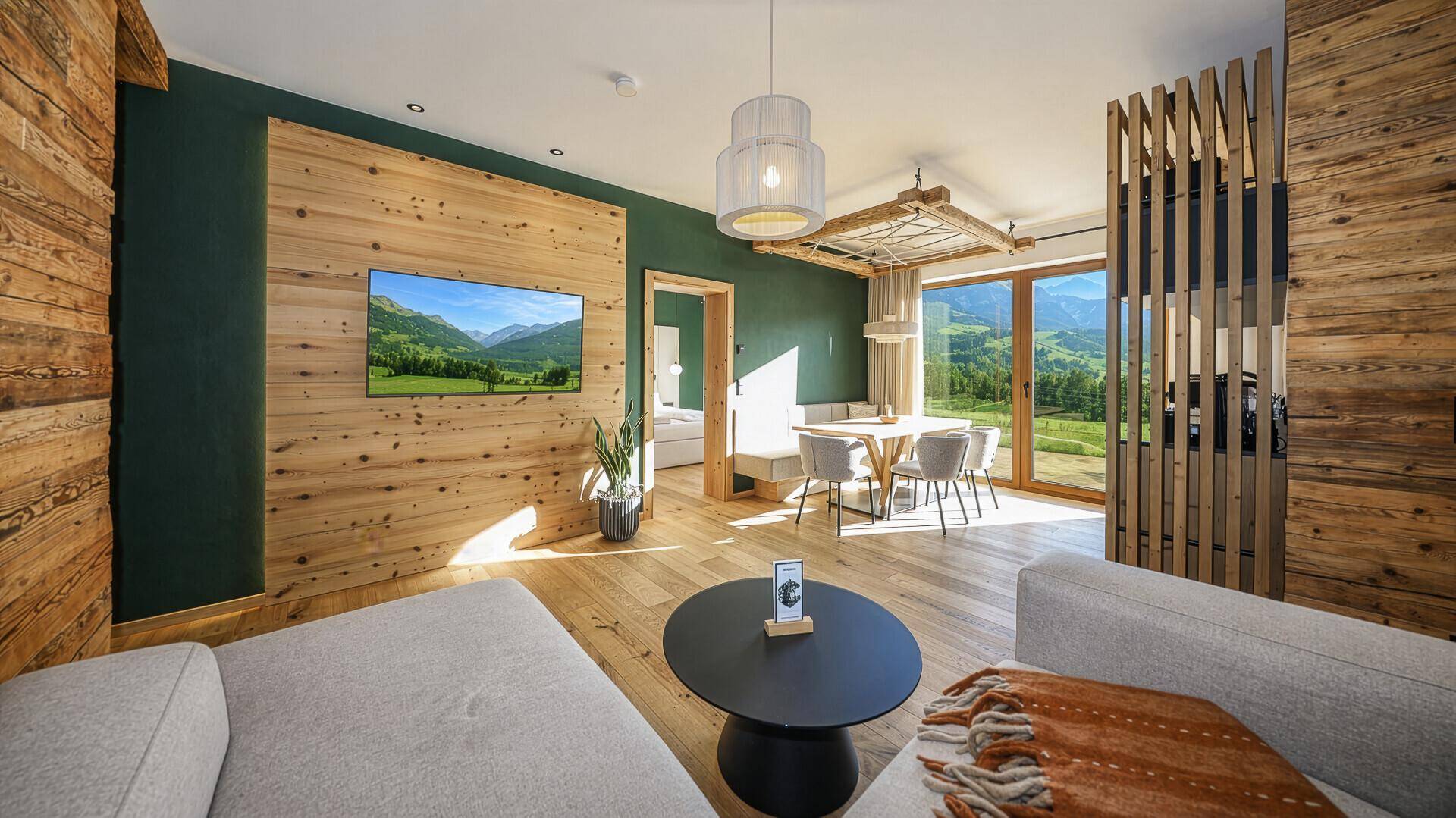 Gemütlicher Wohn-Essbereich mit Holzwänden, modernem Sofa und atemberaubendem Bergblick.