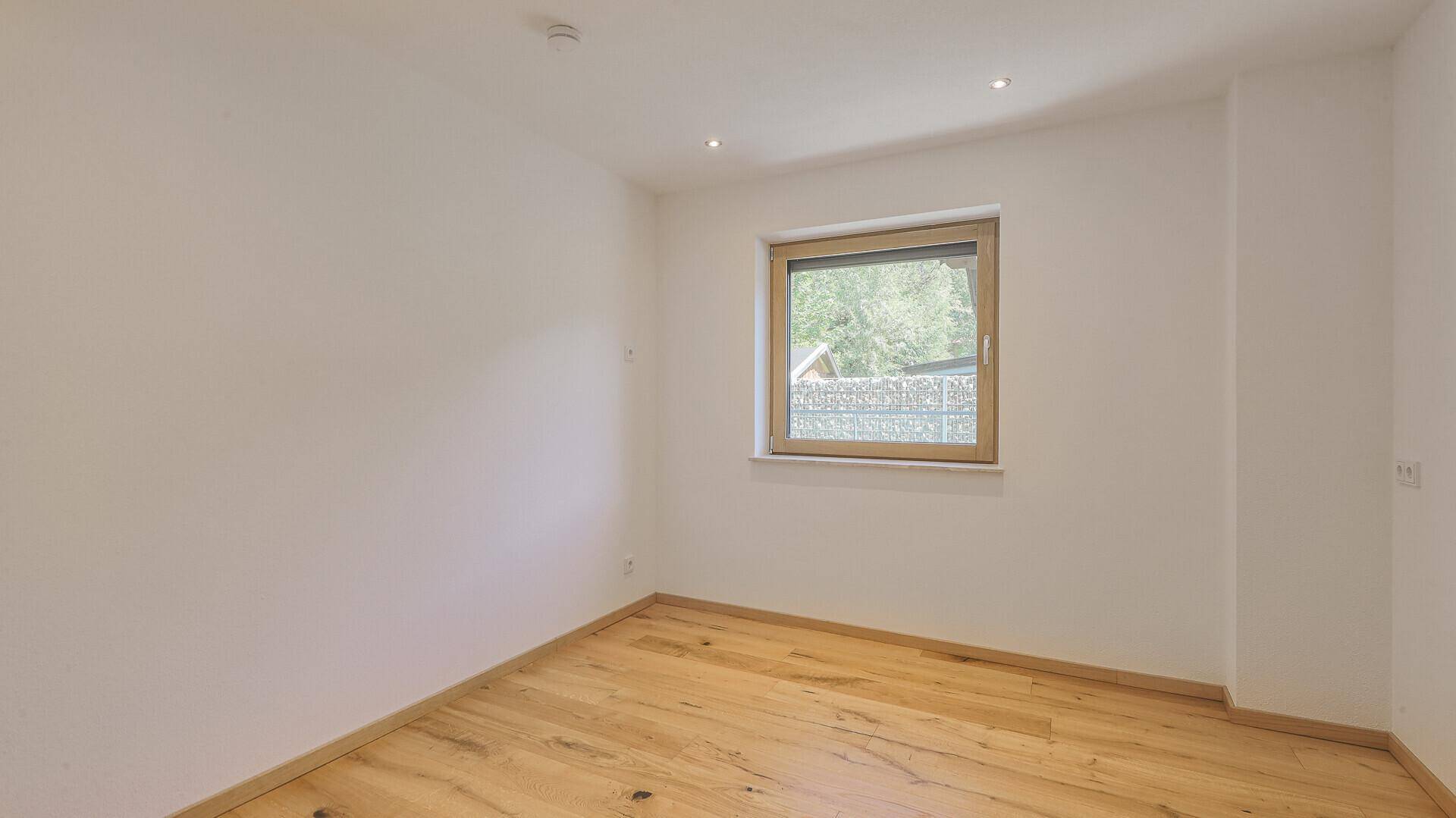 Leeres Schlafzimmer mit Holzboden, weiß gestrichenen Wänden und Fenster.