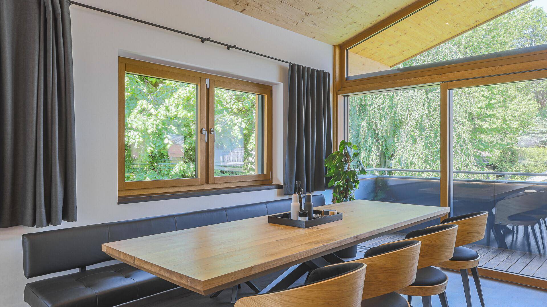 Heller Essbereich mit Holztisch, Sitzbank und großen Fenstern mit Blick ins Grüne.