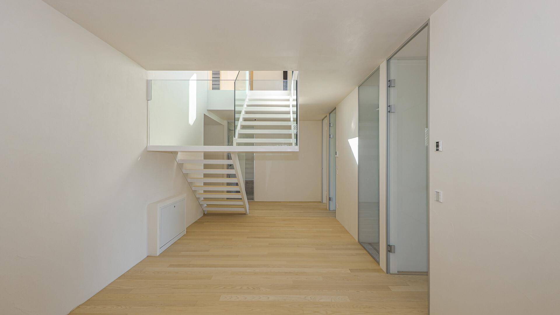 Moderner Flur mit offener Treppe, Glasgeländer und Holzboden.