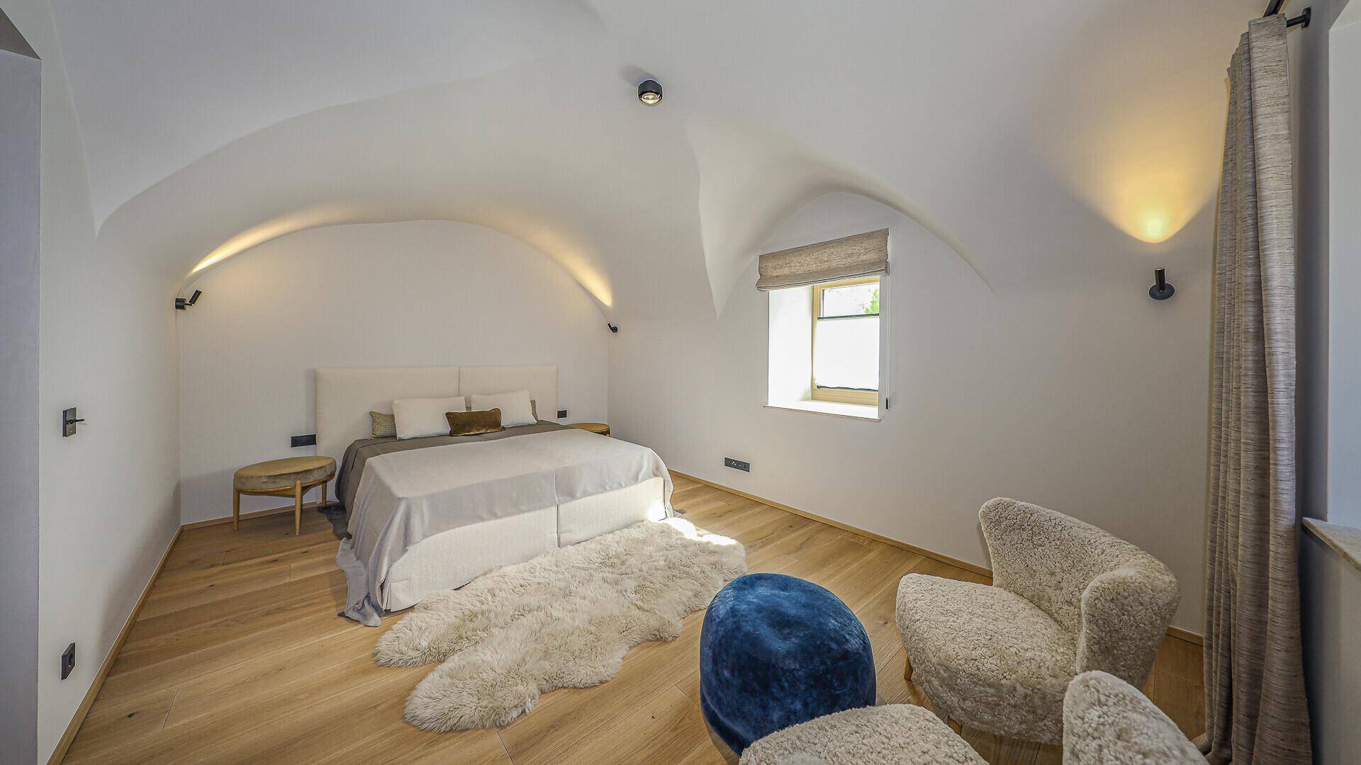 Helles Schlafzimmer mit gewölbter Decke, Holzboden und gemütlicher Sitzecke.