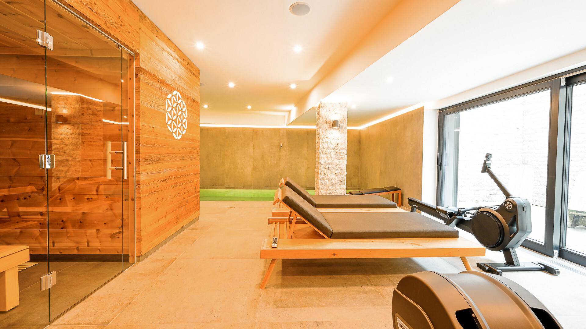Wellnessbereich mit Sauna, Liegestühlen und Fitnessgeräten neben dem Pool.