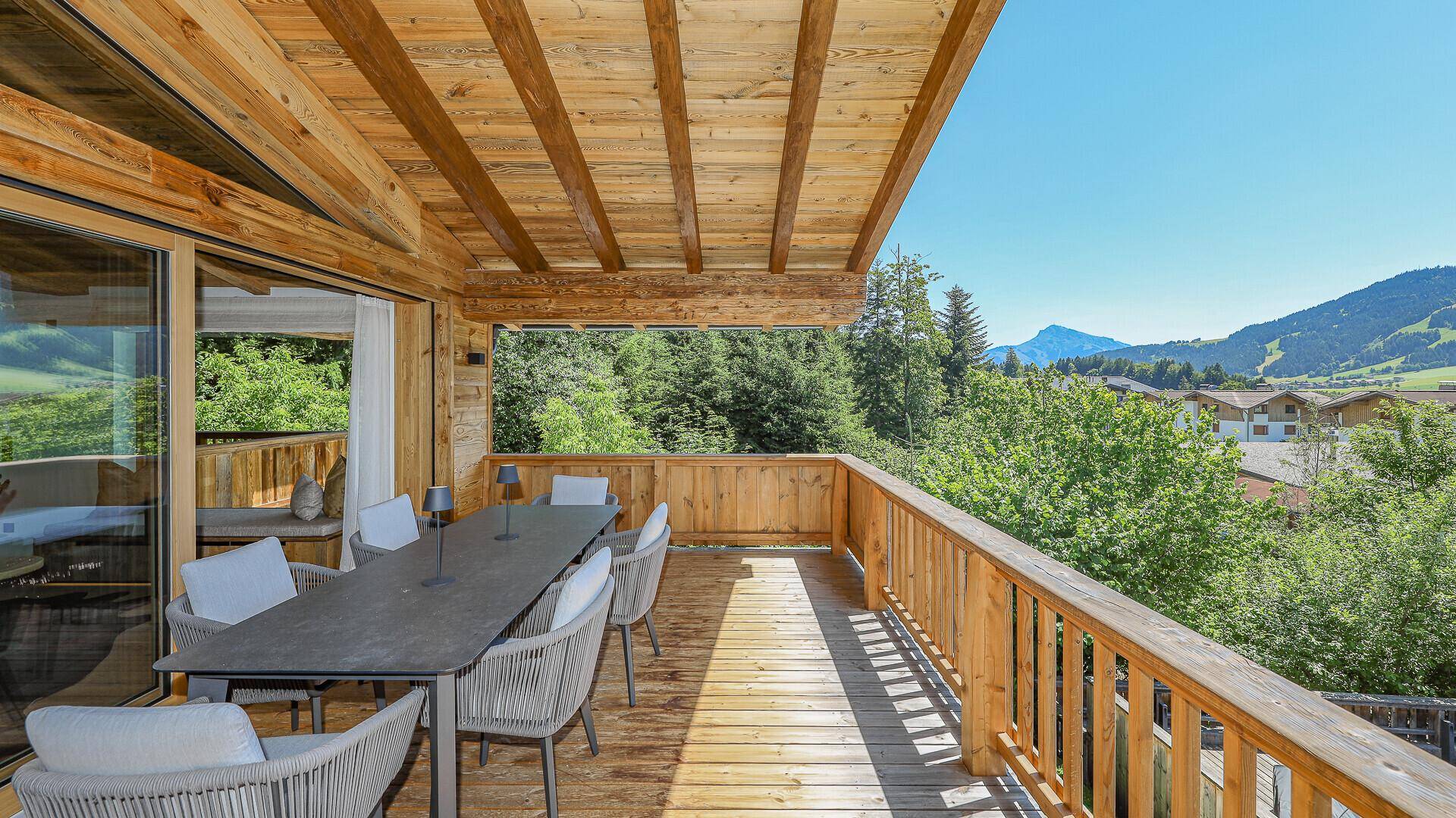 Geräumiger Holzbalkon mit Essbereich und weitem Blick auf die umliegende Berglandschaft.