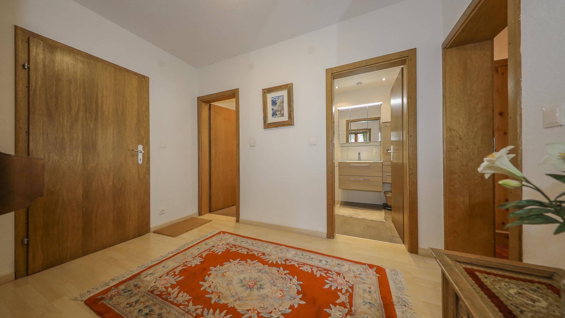Heller Flur mit Holztüren, Teppich und Blick in ein modernes Badezimmer.