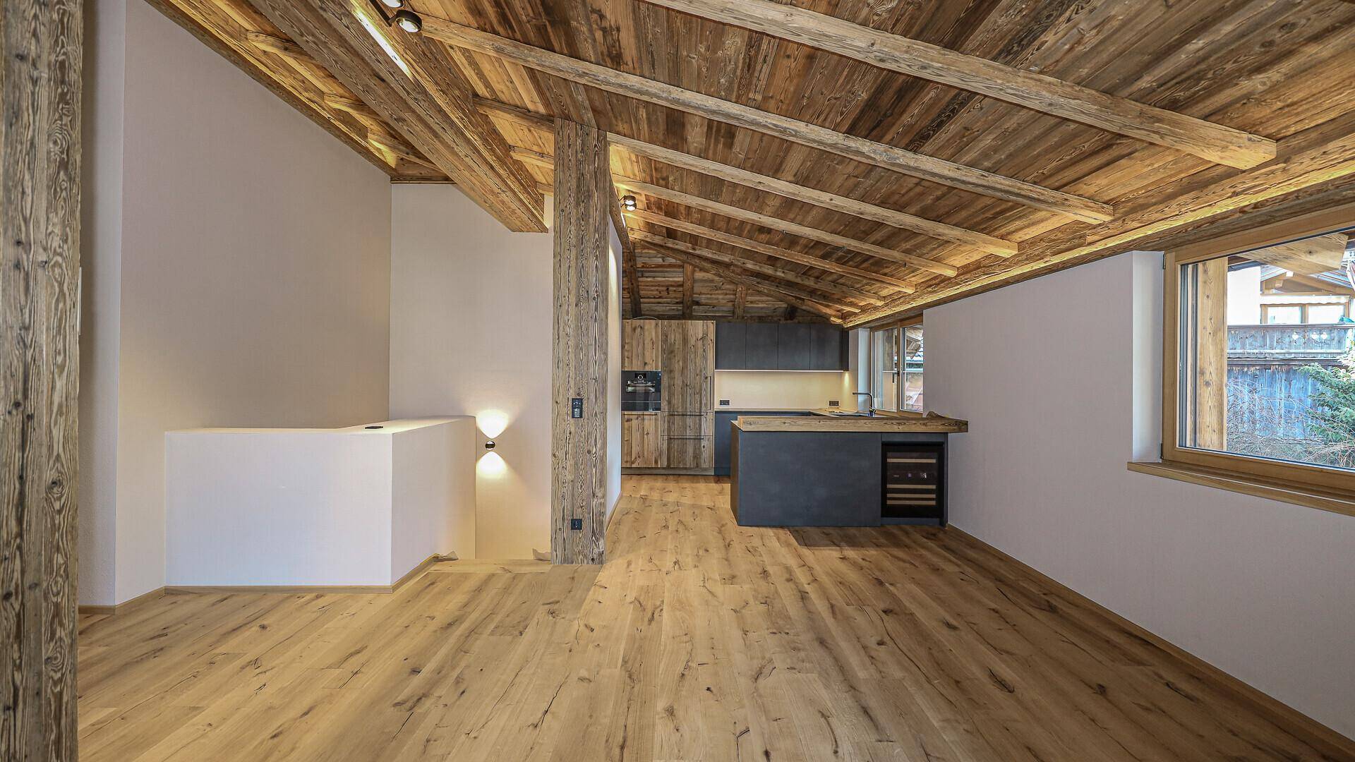 Offener Wohnbereich mit Holzbalkendecke, Holzboden und integrierter Küche.