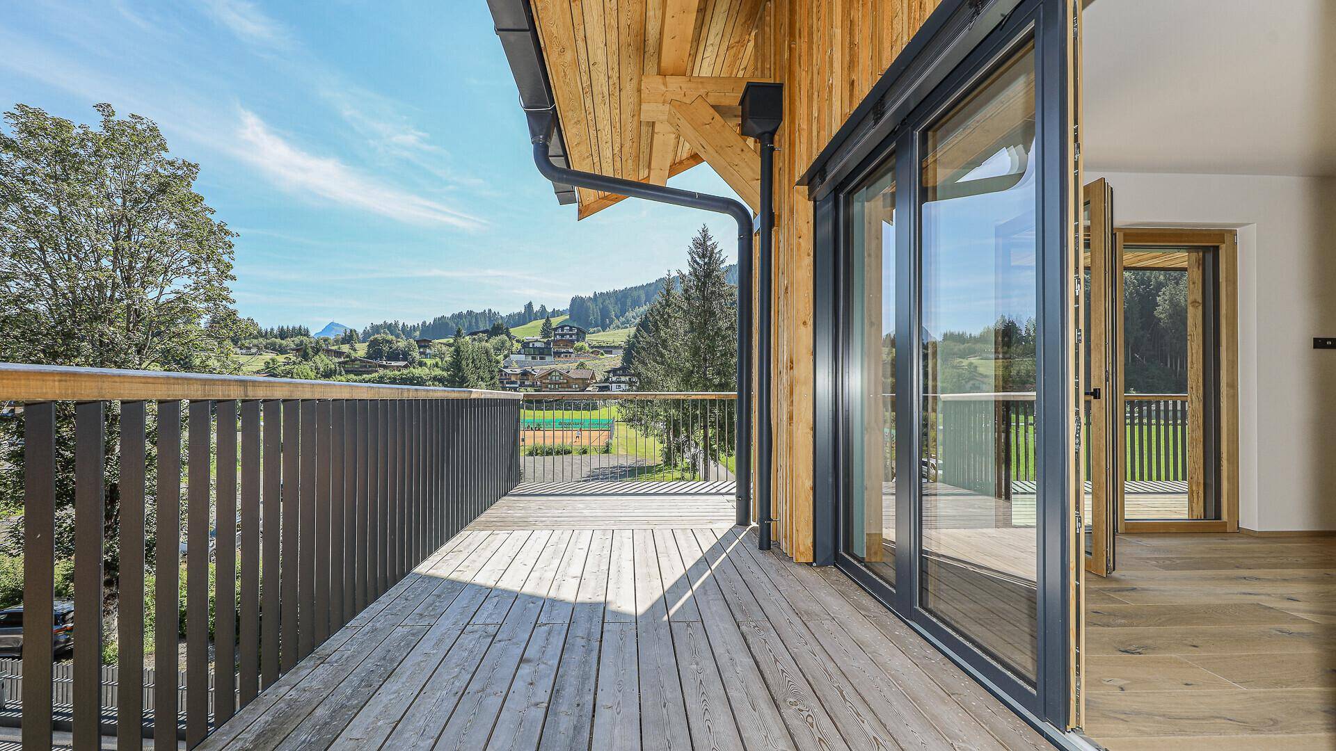 Geräumiger Holzbalkon mit Blick auf die grüne Landschaft und die umliegenden Gebäude.