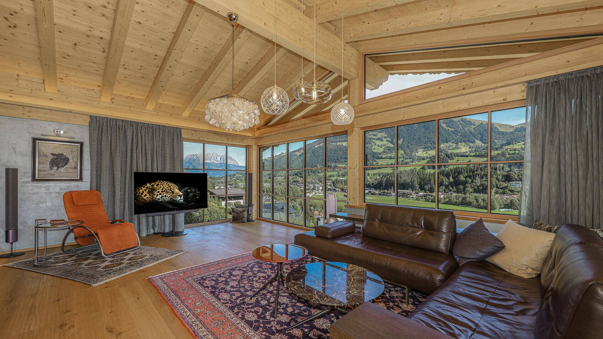 Helles Wohnzimmer mit bequemen Ledersofas, Holzboden und Panoramablick auf die Berge.