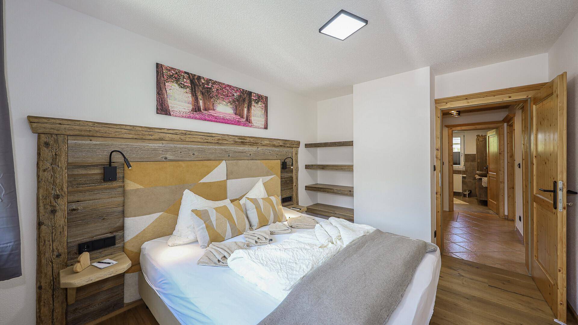 Schlafzimmer mit Doppelbett, Holzelementen und Zugang zu einem angrenzenden Raum.