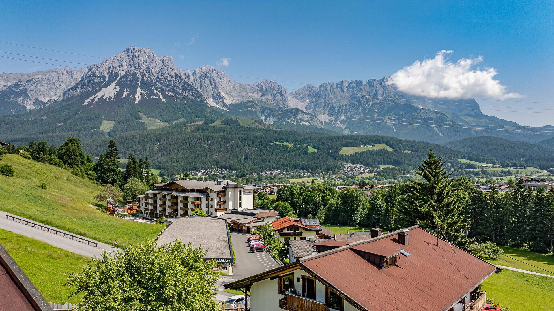 Weitläufiger Blick auf eine alpine Landschaft mit Bergen, Wäldern und einer kleinen Siedlung.