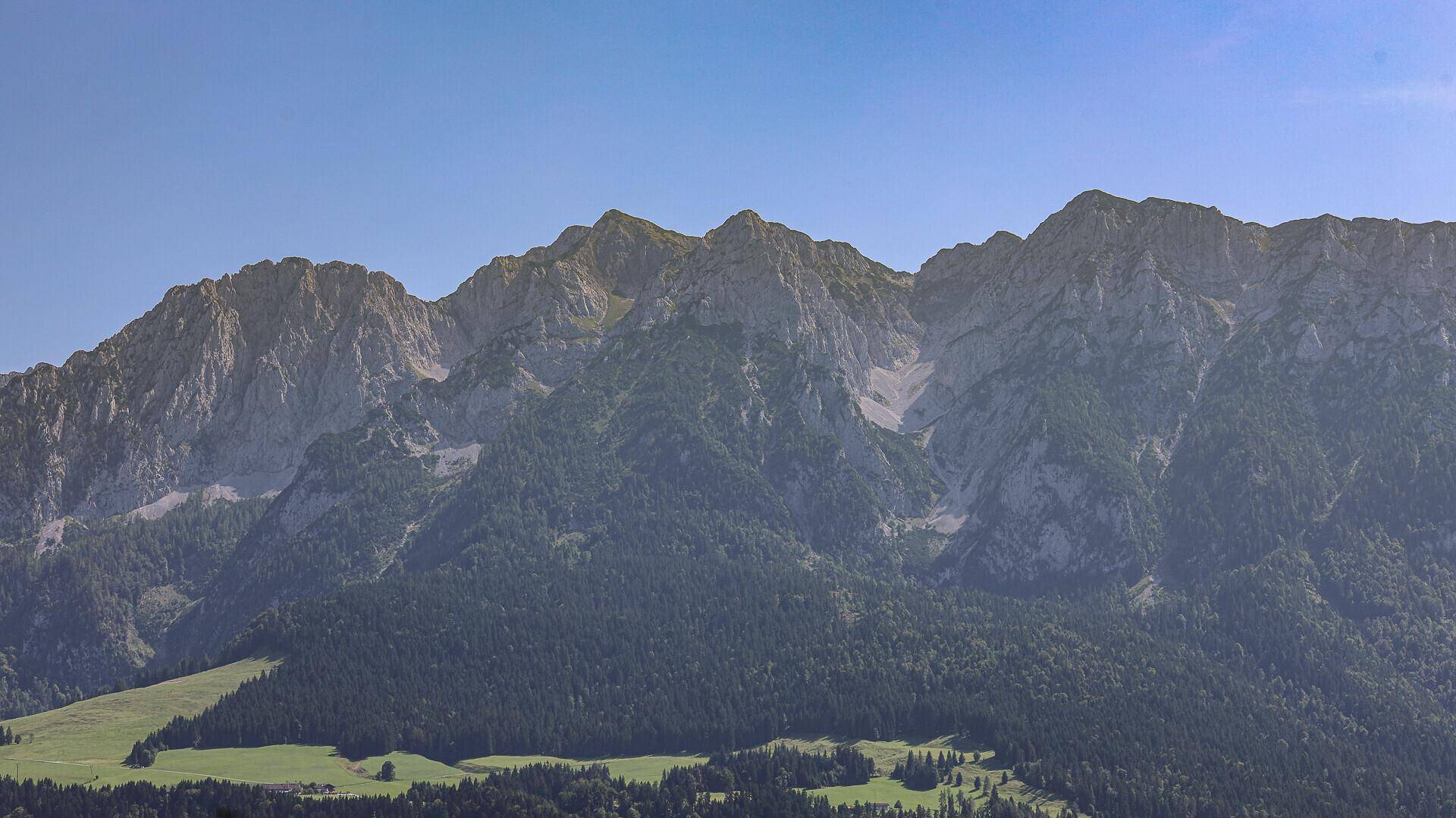 Majestätische Bergkette mit bewaldeten Hängen und schroffen Felsgipfeln unter klarem Himmel.