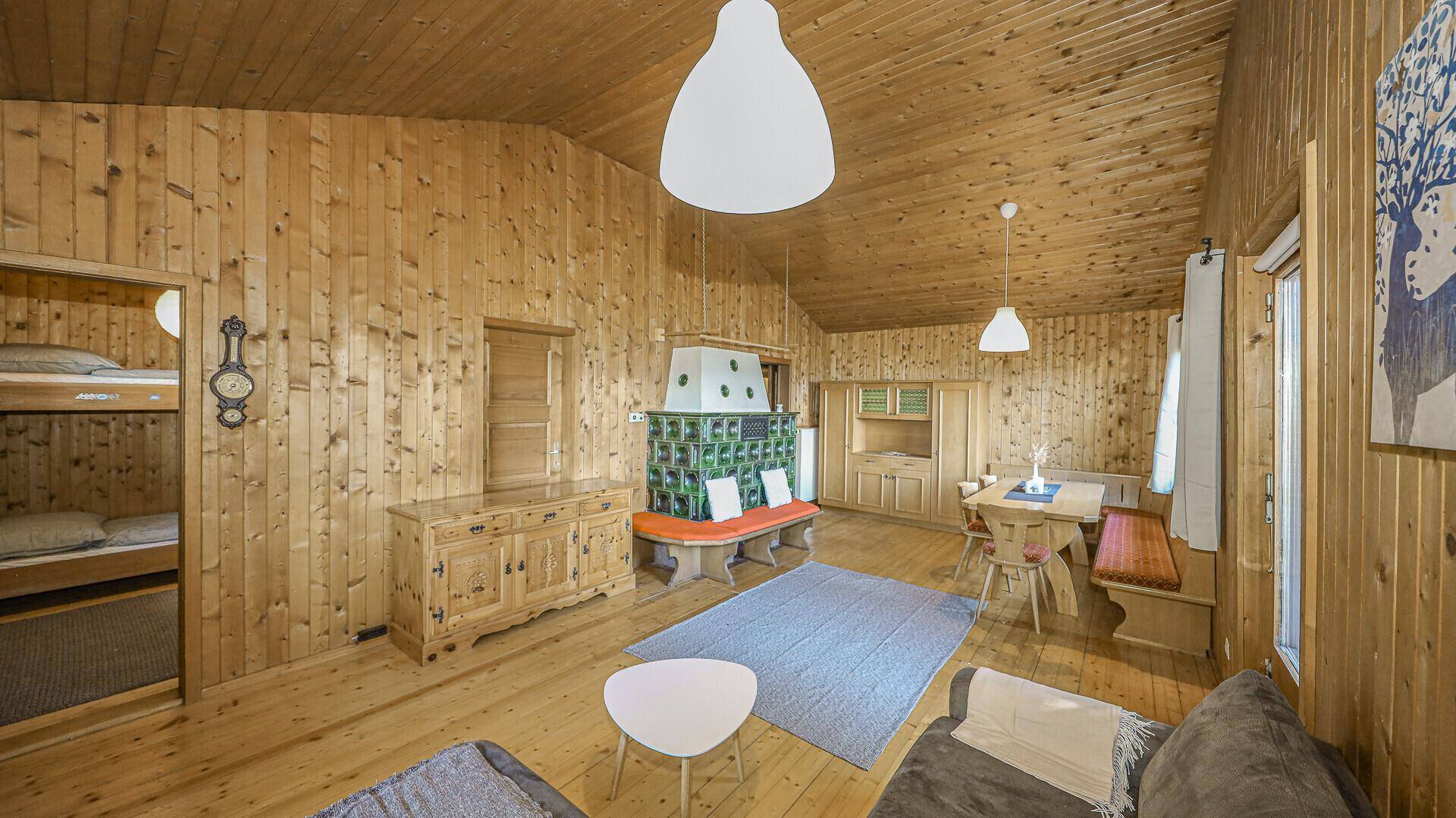 Traditioneller Wohn-Essbereich mit Holzvertäfelung, Kachelofen und Zugang zu einem Schlafzimmer.