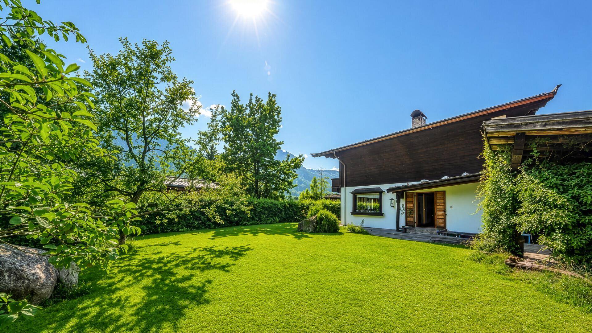 Sonniger Gartenbereich mit weitläufigem Rasen und Blick auf die umliegenden Berge.