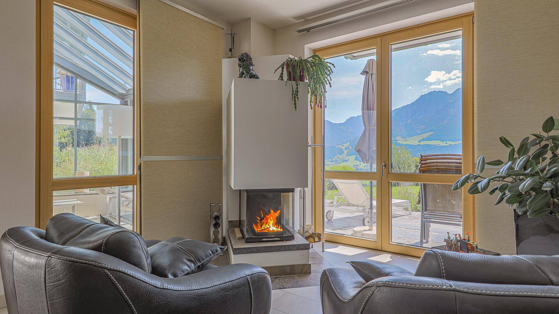 Gemütliches Wohnzimmer mit Kamin und großen Fenstern, die einen schönen Blick ins Grüne bieten.